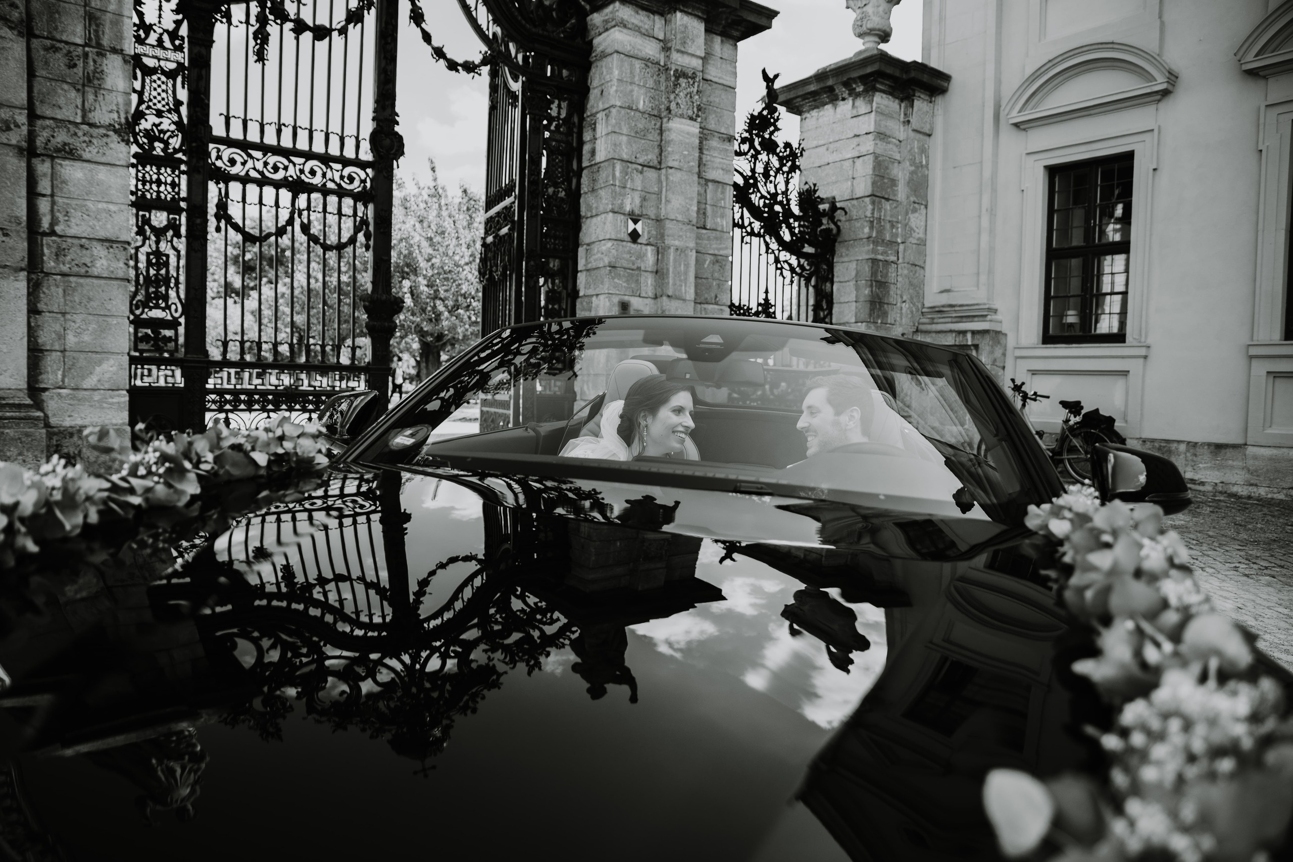 Braut und Bräutigam sitzen im Hochzeitscabriolet im Hof der Residenz Würzburg.