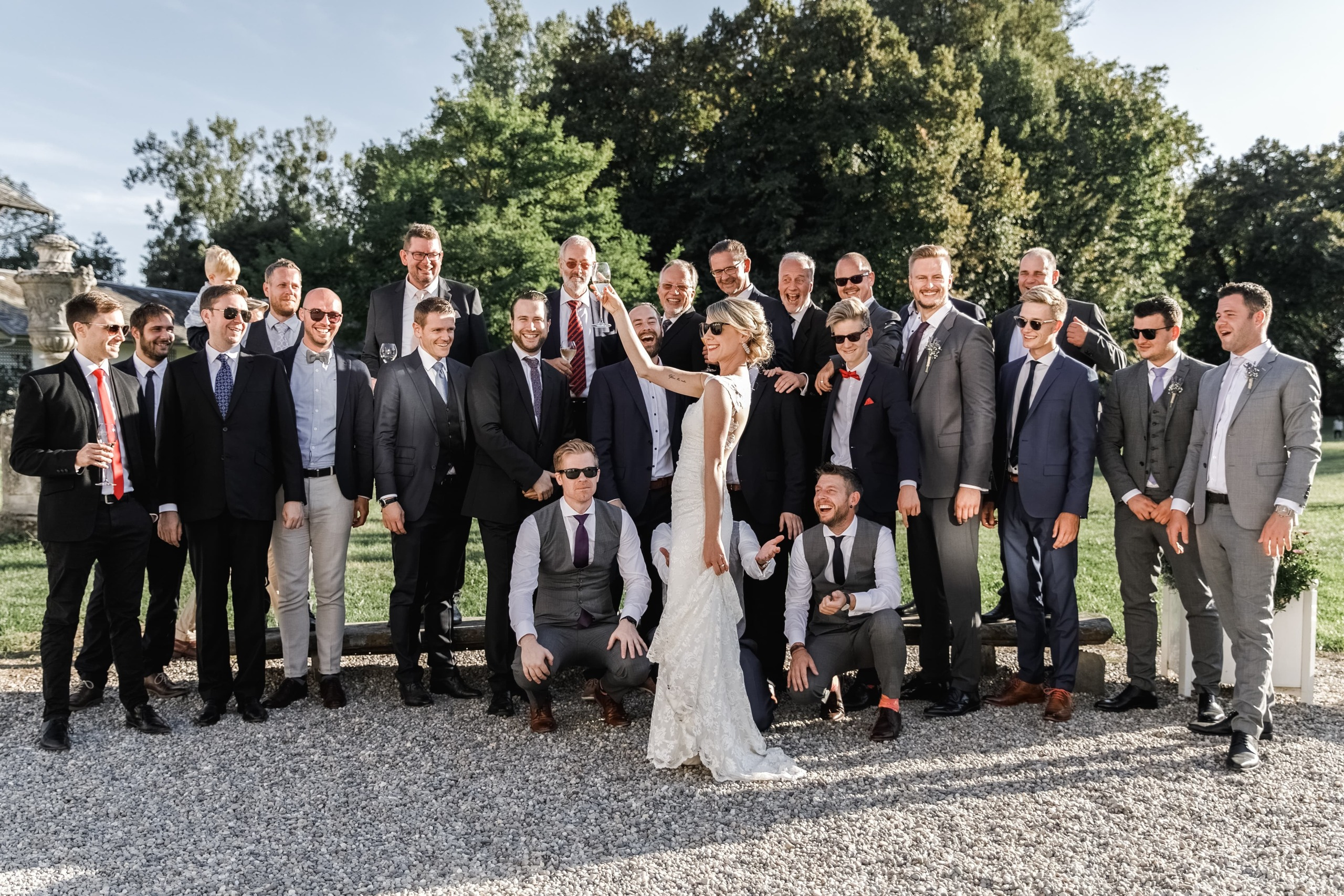 Freunde des Bräutigams blicken lächelnd auf die Braut mit Champagnerglas.