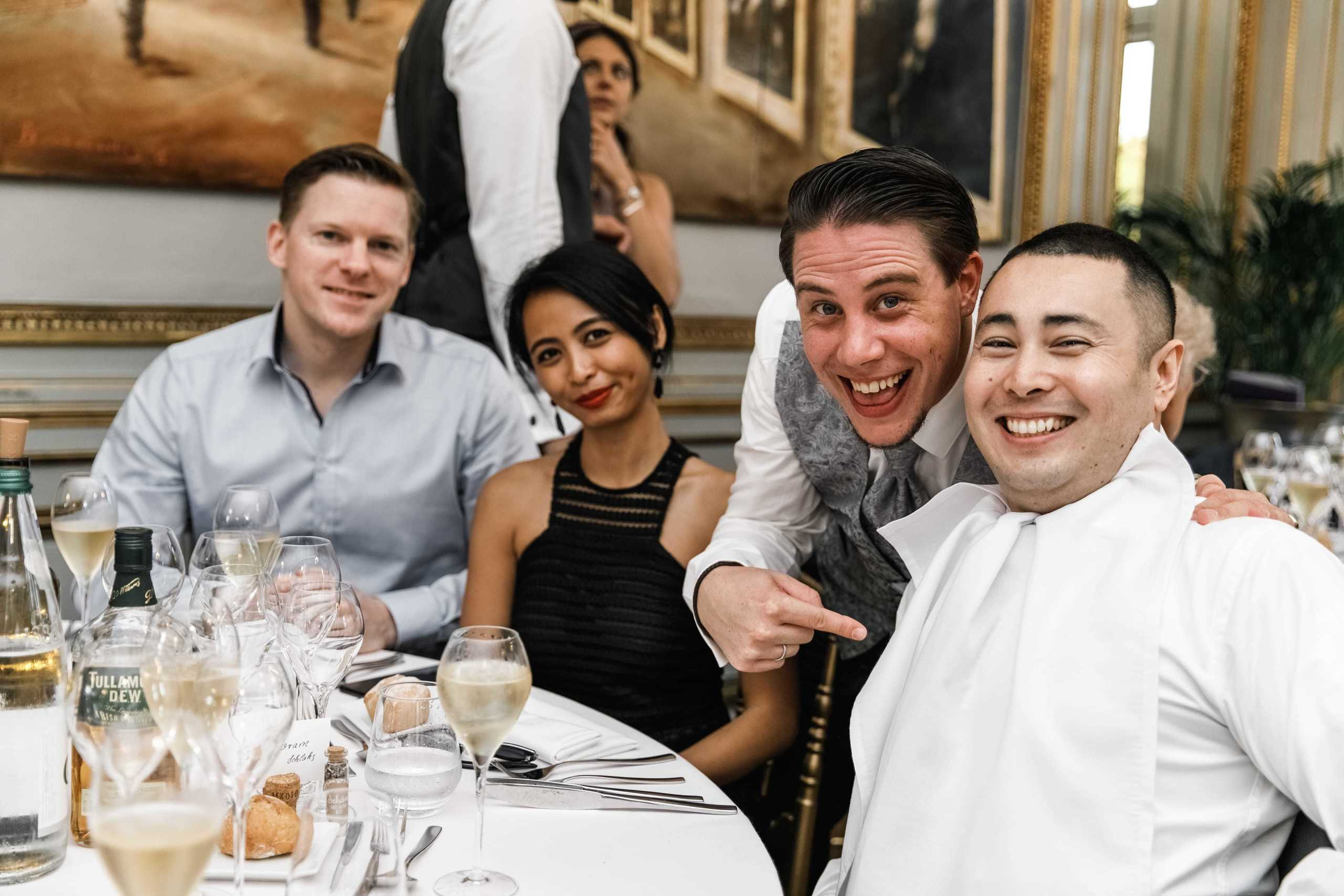 Bräutigam lacht und lächelt mit Hochzeitsgästen über das Lätzchen, das ein Gast gemacht hat.