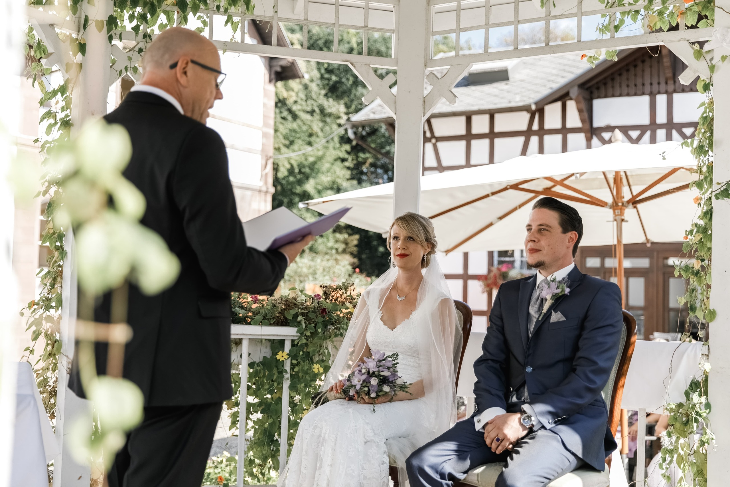 Braut und Bräutigam schauen aufmerksam auf den Trauredner während der Zeremonie.