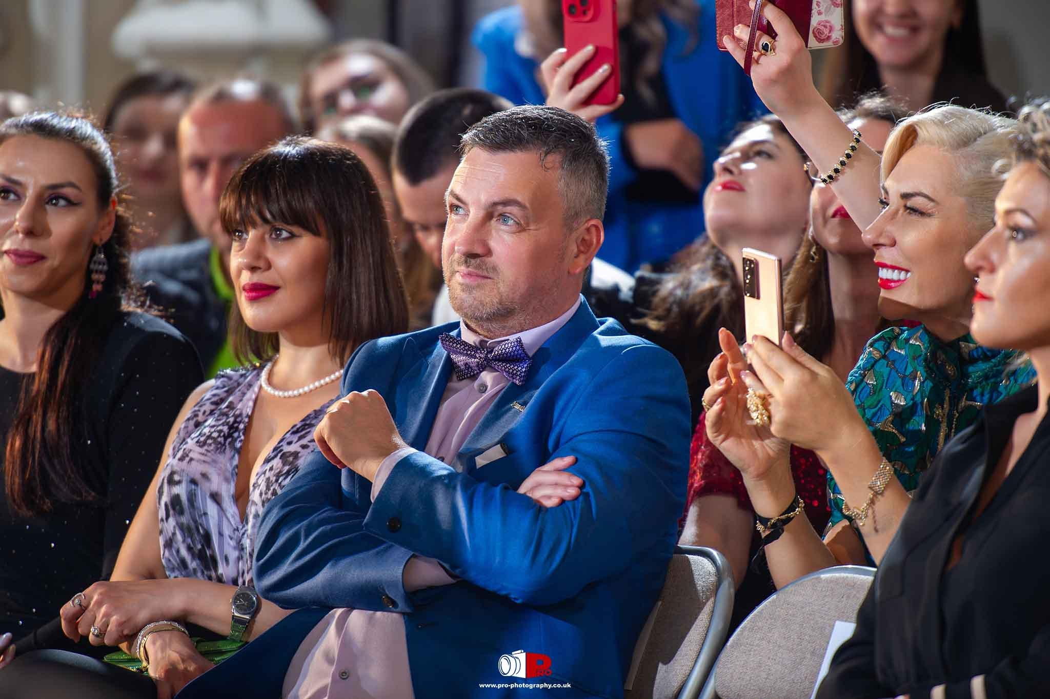 Engaged audience members watching and recording the fashion show with phones, showcasing a lively and supportive atmosphere.