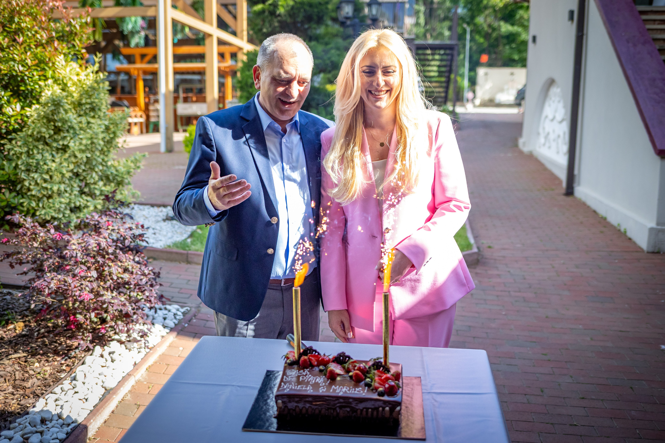 Proaspăt căsătoriții râd în fața tortului de cununie, luminat de artificii festive în grădina Restaurantului Diesel din București.
