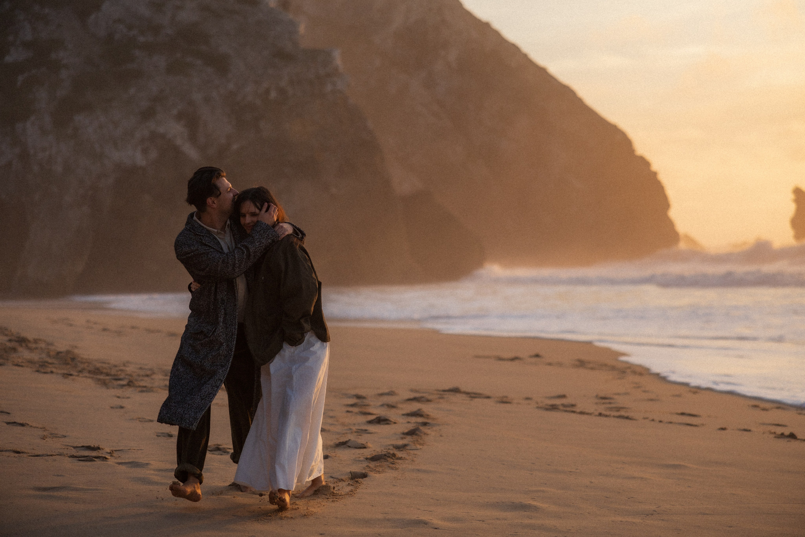 Couple holding hands and walking through a picturesque coastline in Portugal.