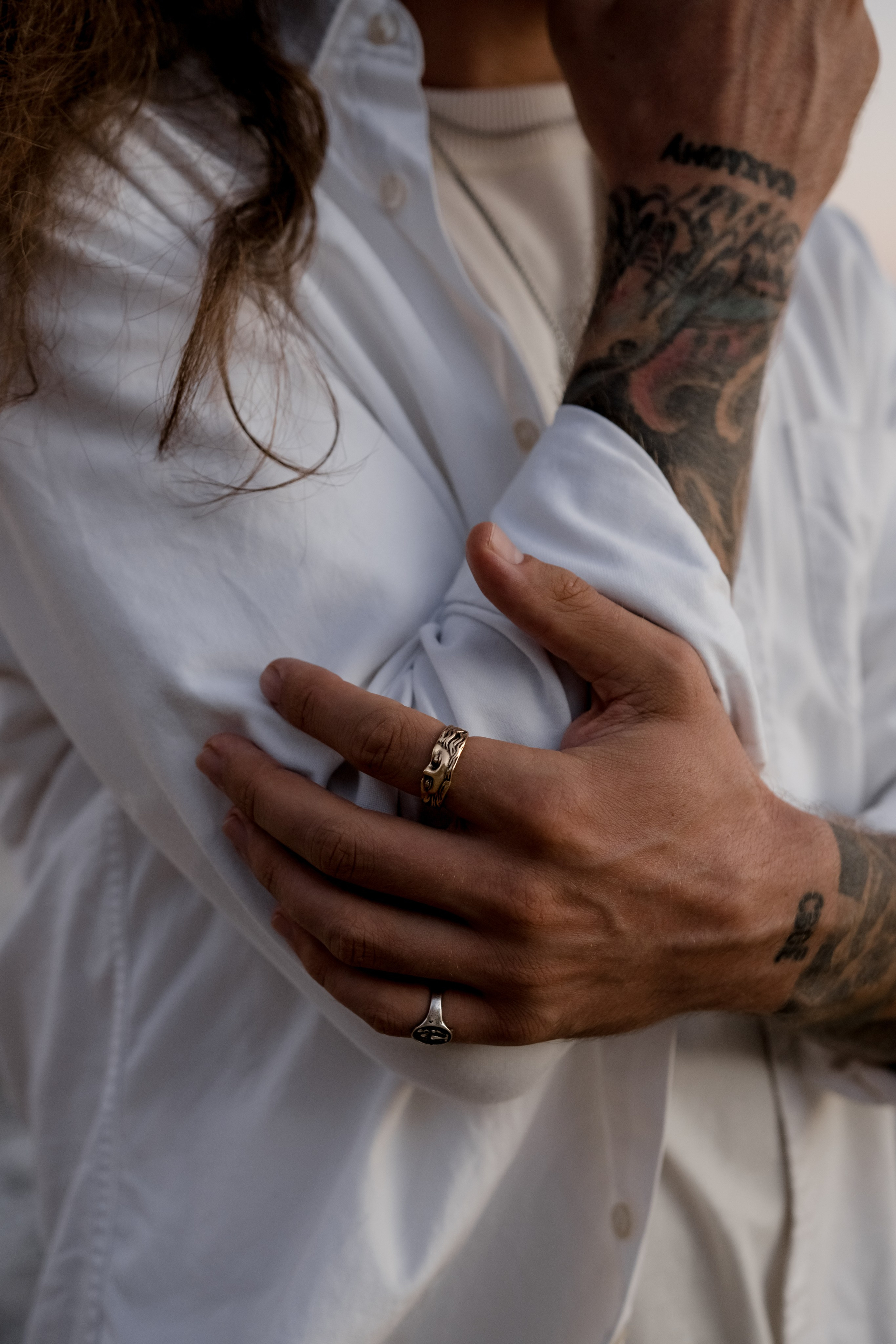 Male model resting his tattooed hands on his chest, emphasizing natural style and intricate jewelry.