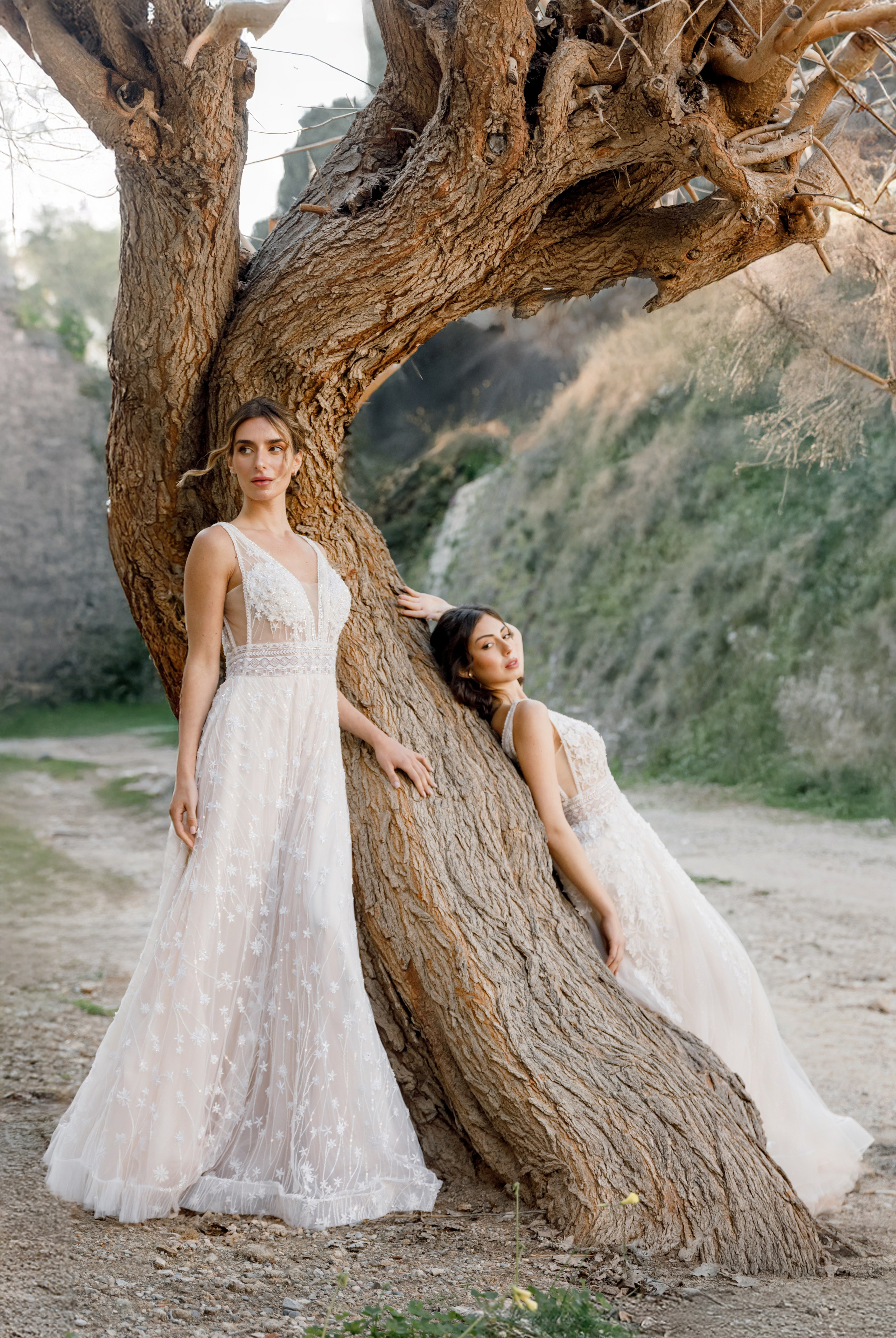 Two brides in elegant wedding dresses pose in the narrow, cobblestone streets of Rhodes' Old Town, surrounded by historic stone buildings and vibrant bougainvillea. The editorial-style photo captures their intimate connection and the timeless charm of the medieval setting, with soft natural light enhancing the romantic atmosphere.