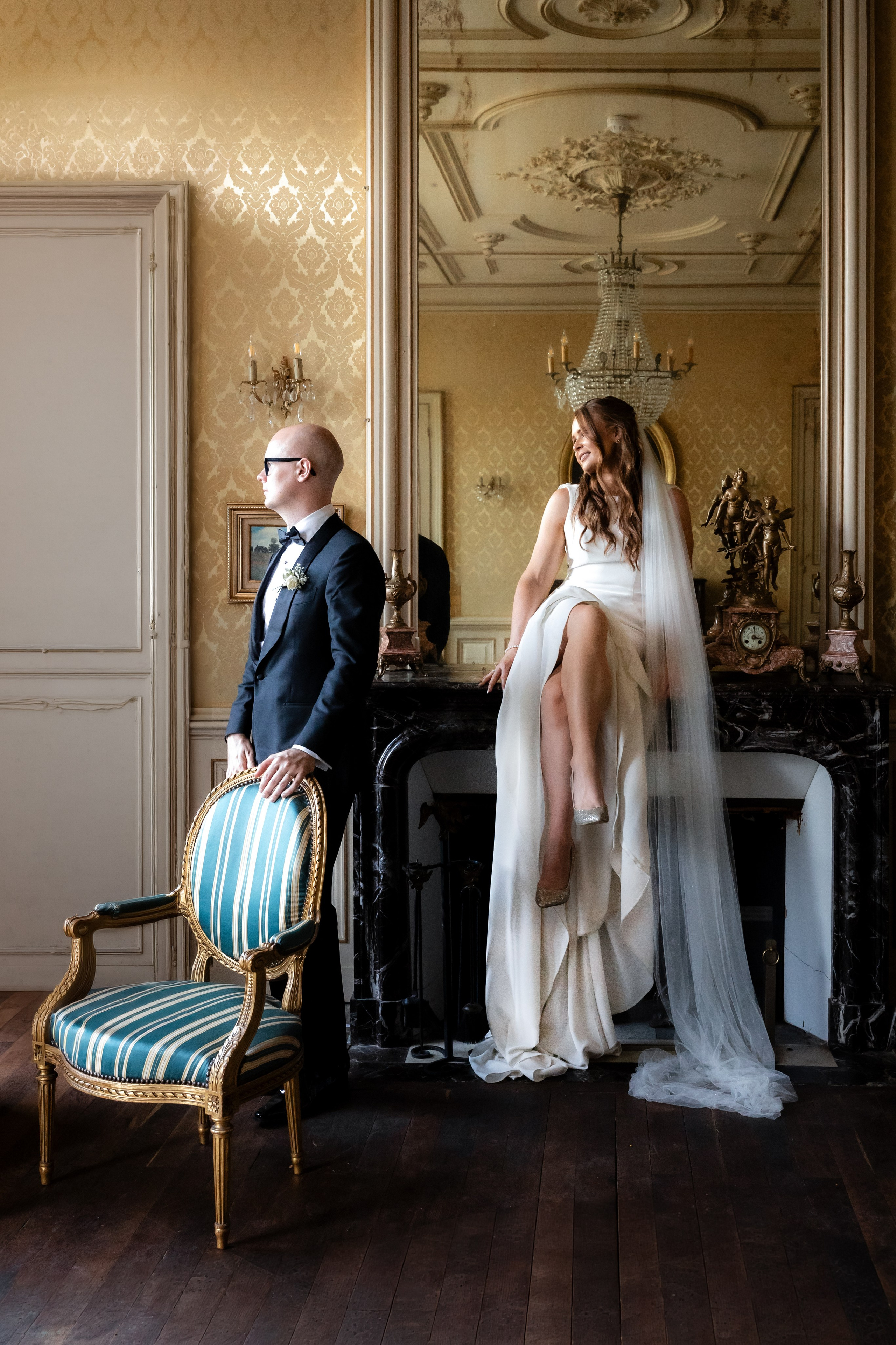 Bride and groom in an ornate château salon beside a gilt mirror