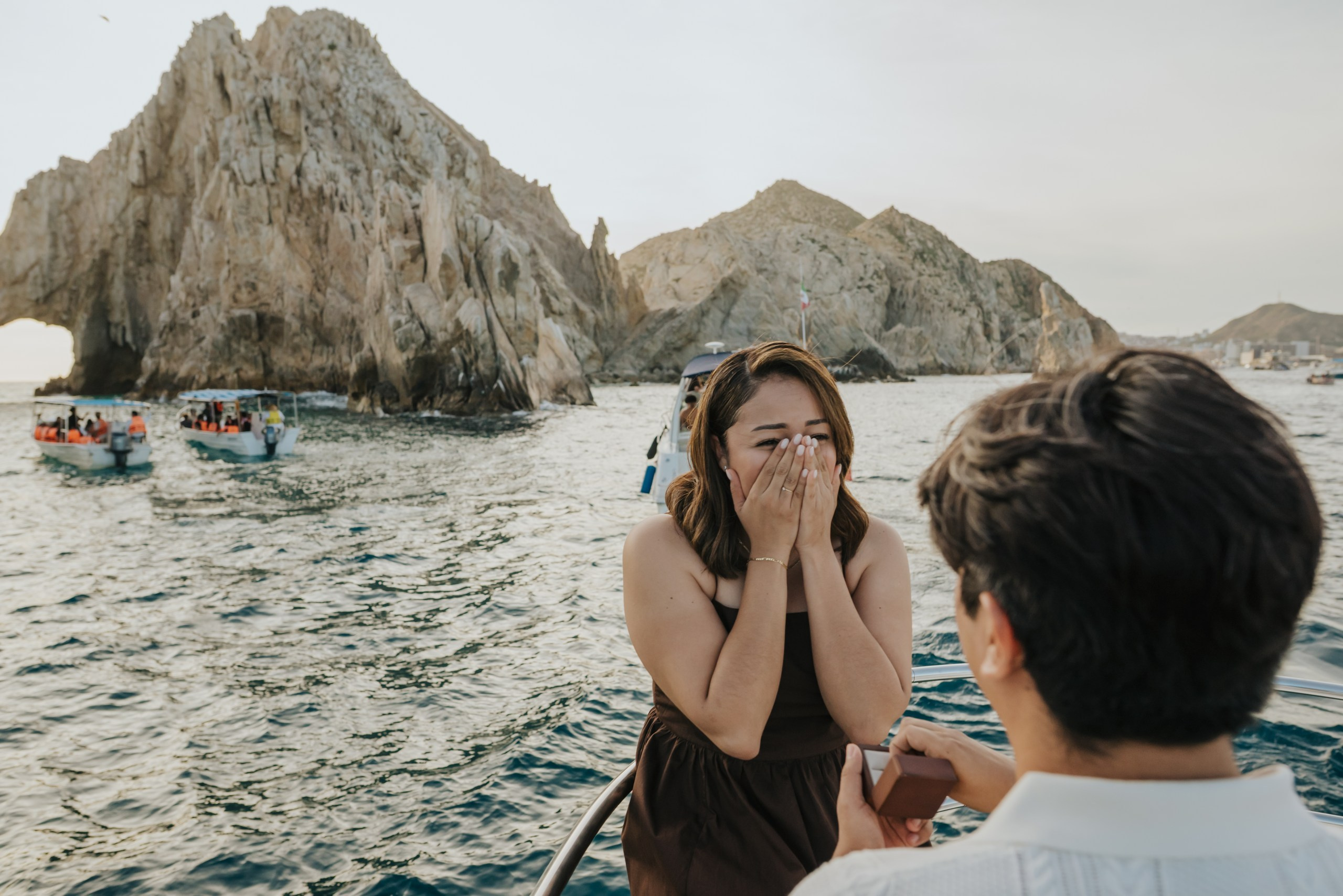 proposal surprise in front of the Arch - groom on one knee on a yacht  with the arch background , romantic experience proposal photography in cabo san lucas