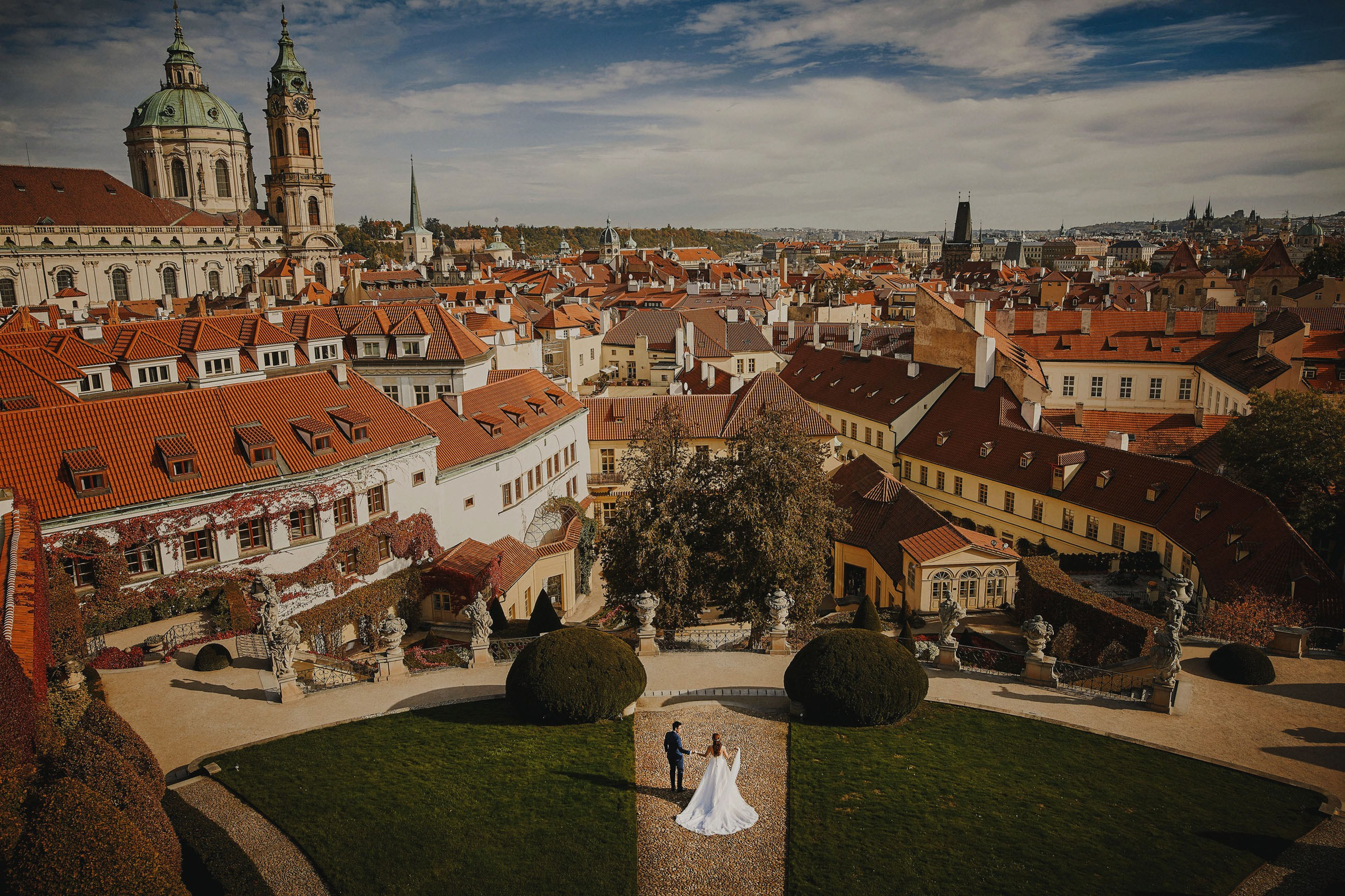 Bird's-eye view of bride and groom in Vrtba Garden with Prague Castle in background.
