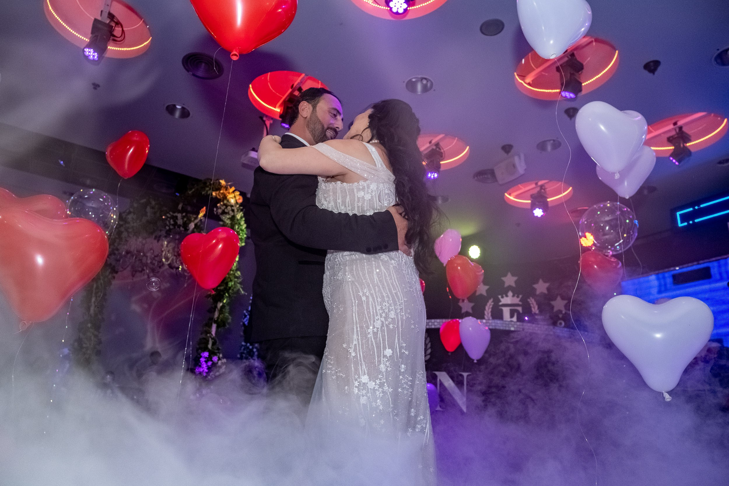 Sara and Emil dance together surrounded by low-lying smoke and heart-shaped balloons