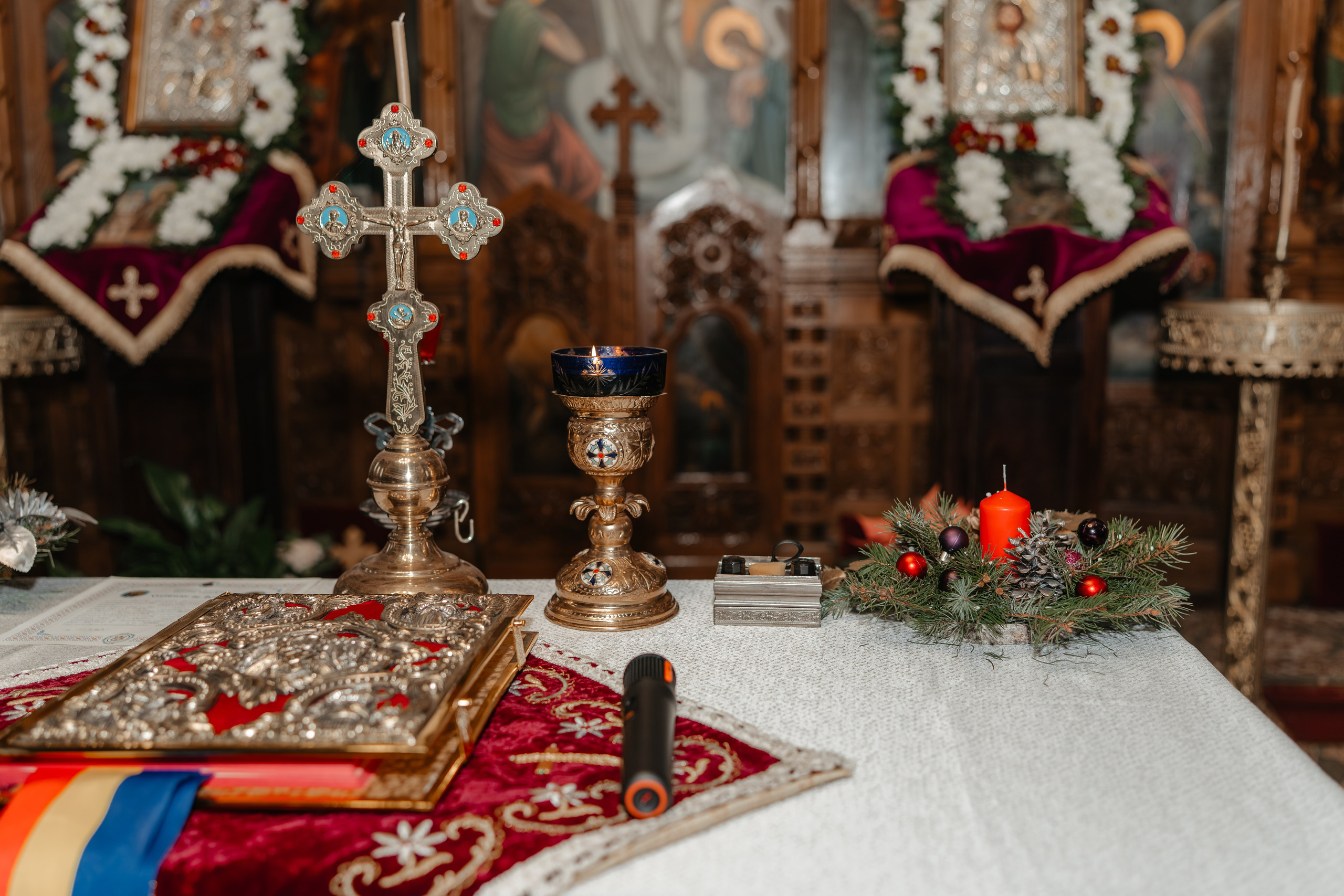 Detaliu solemn de la botez: o Biblie veche, o cruce și obiecte ornamentale bisericești așezate pe un altar în Biserica Grivița, Vaslui. Fotografie artistică de botez.