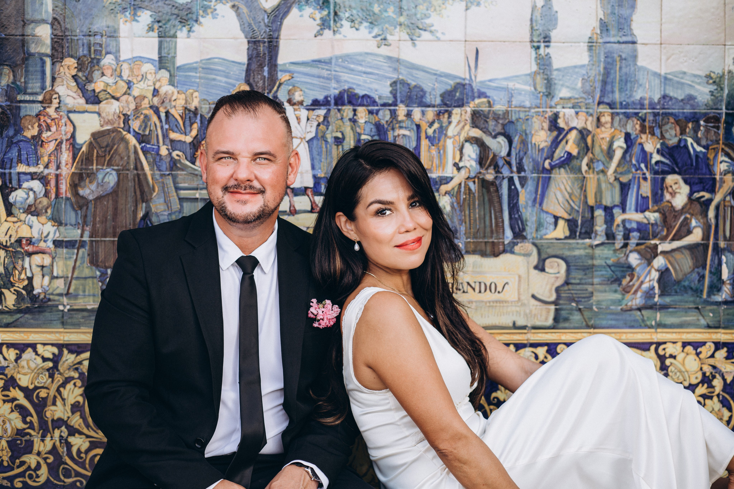 Bride and groom sitting together in front of colorful ceramic tiles at Plaza de España in Sevilla. Elegant portrait from their intimate destination wedding in Andalusia.