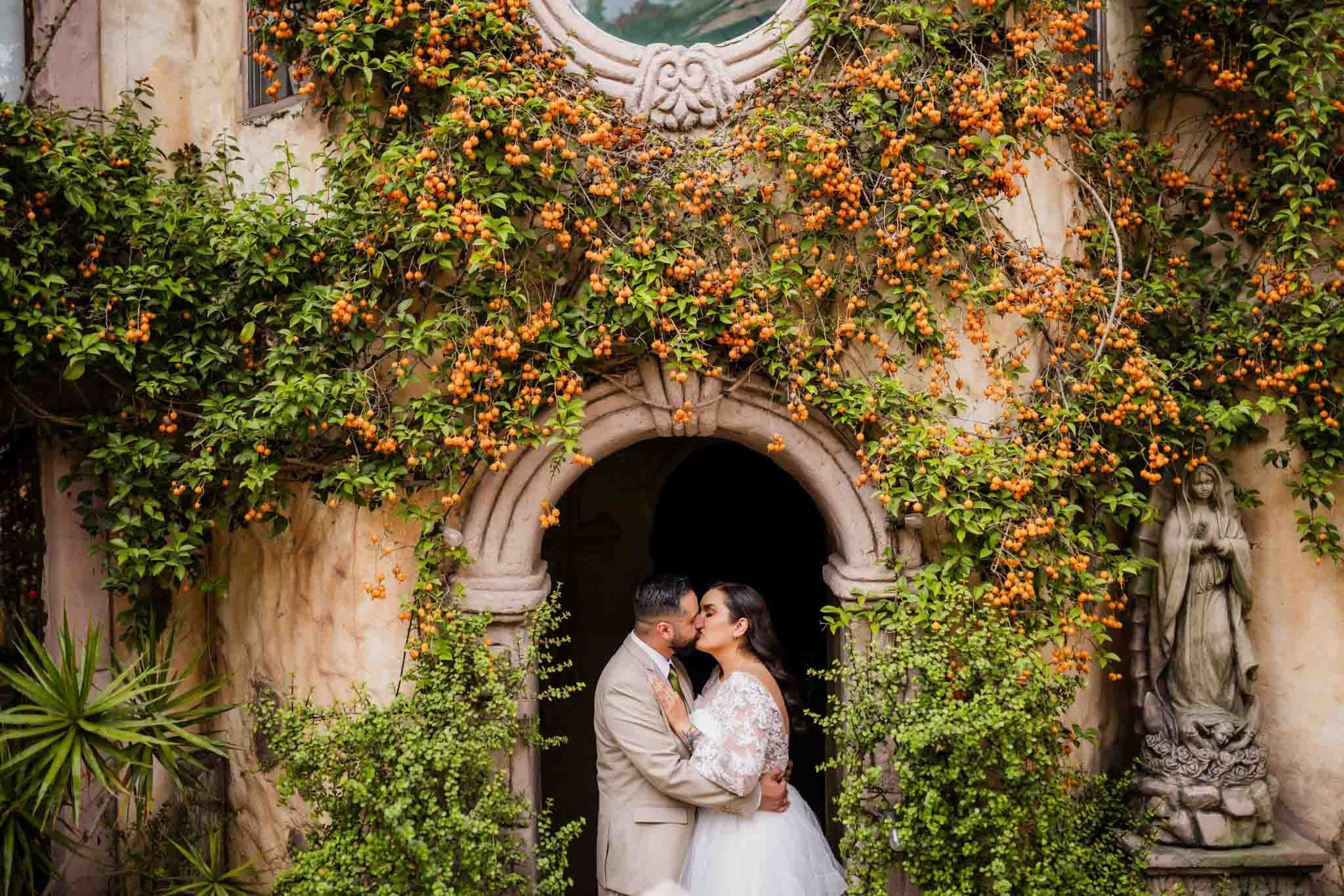 Fotografía de boda en Jardín Casa Baga Rosarito, novios besándose bajo arco con enredaderas, fotógrafo de bodas en Tijuana Baja California, sesiones románticas en jardín para bodas destino México