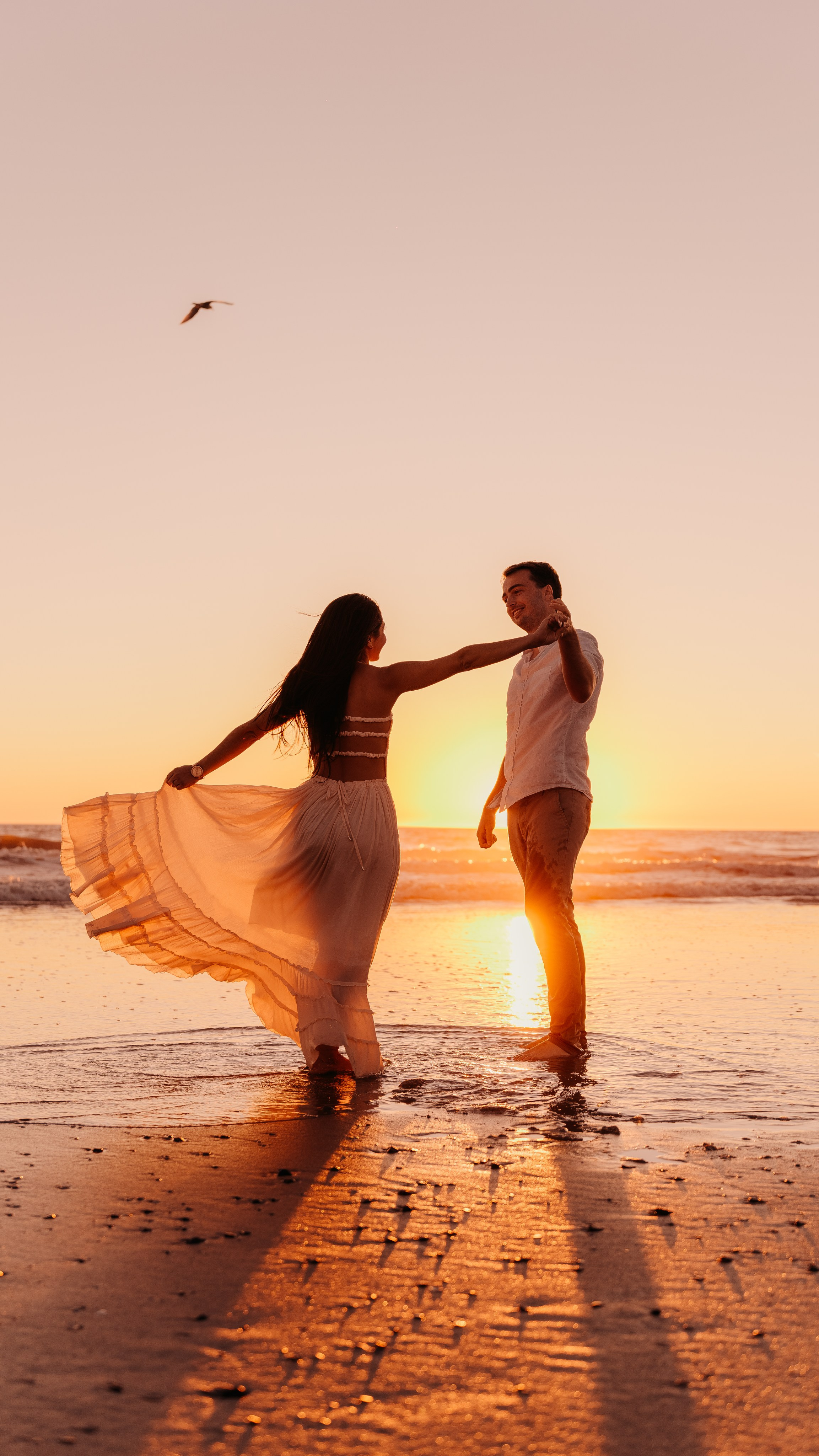 Romantic beach engagement session at sunset with couple, walking along the shoreline, capturing candid moments and natural light 