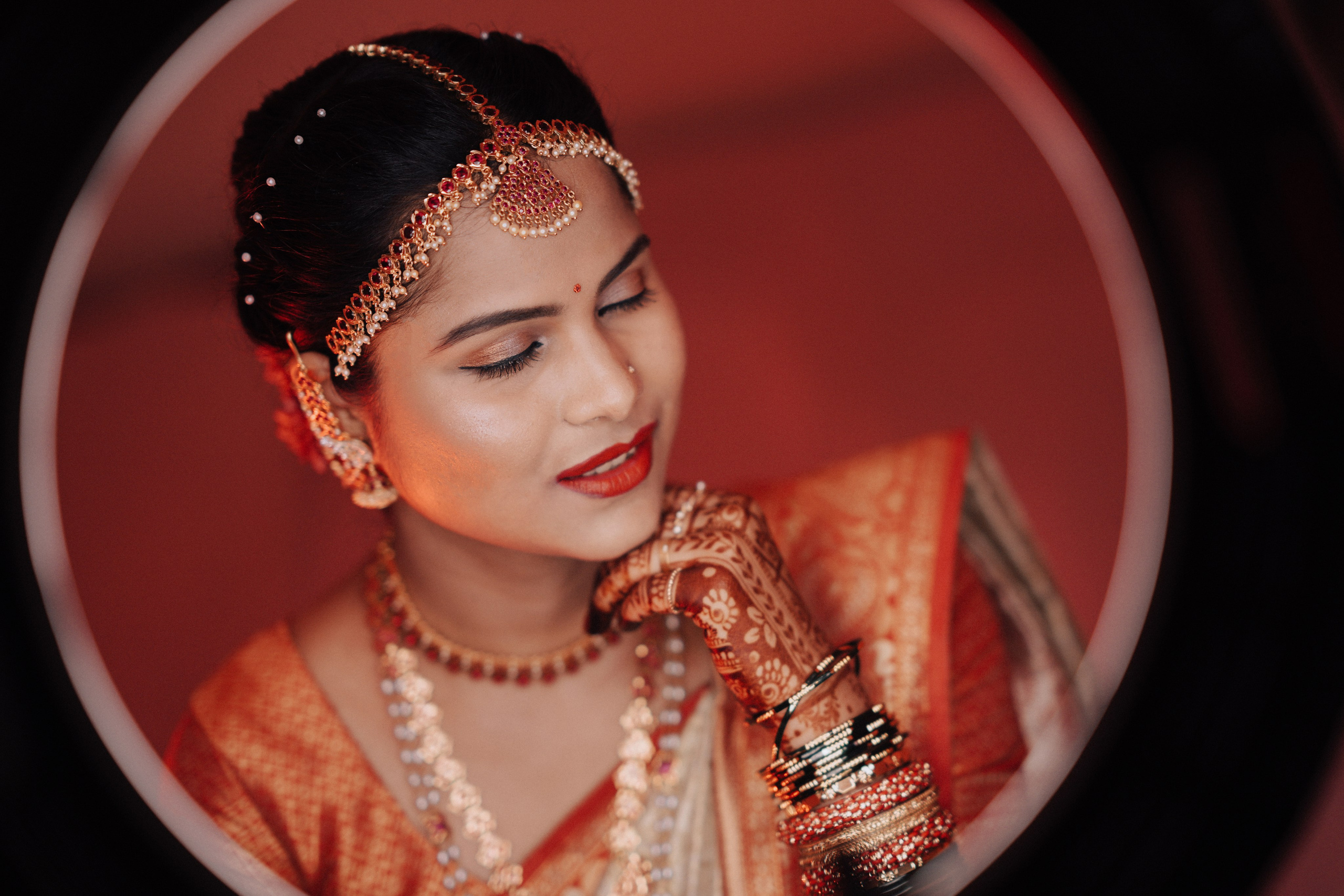 professional studio portrait of a woman wearing a red and gold saree and bridal jewelry posing inside a ring light frame in Malleshwaram, Bengaluru