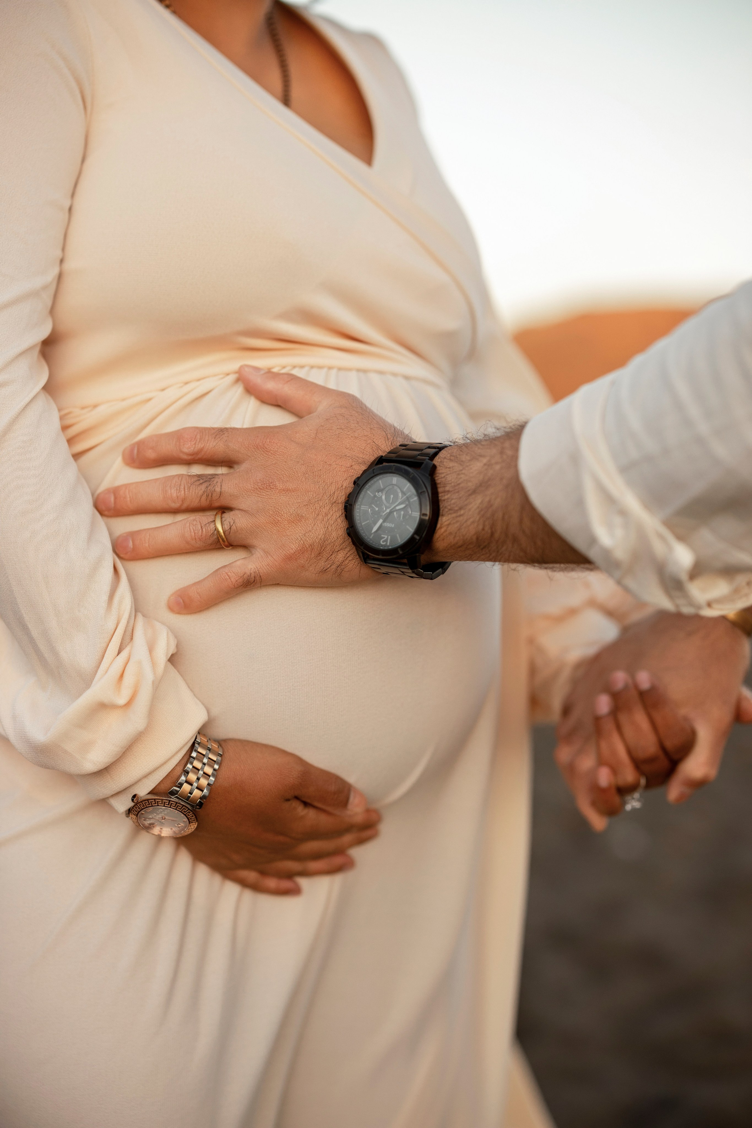 Pregnancy photoshoot at sunset with couple holding hands on the beach