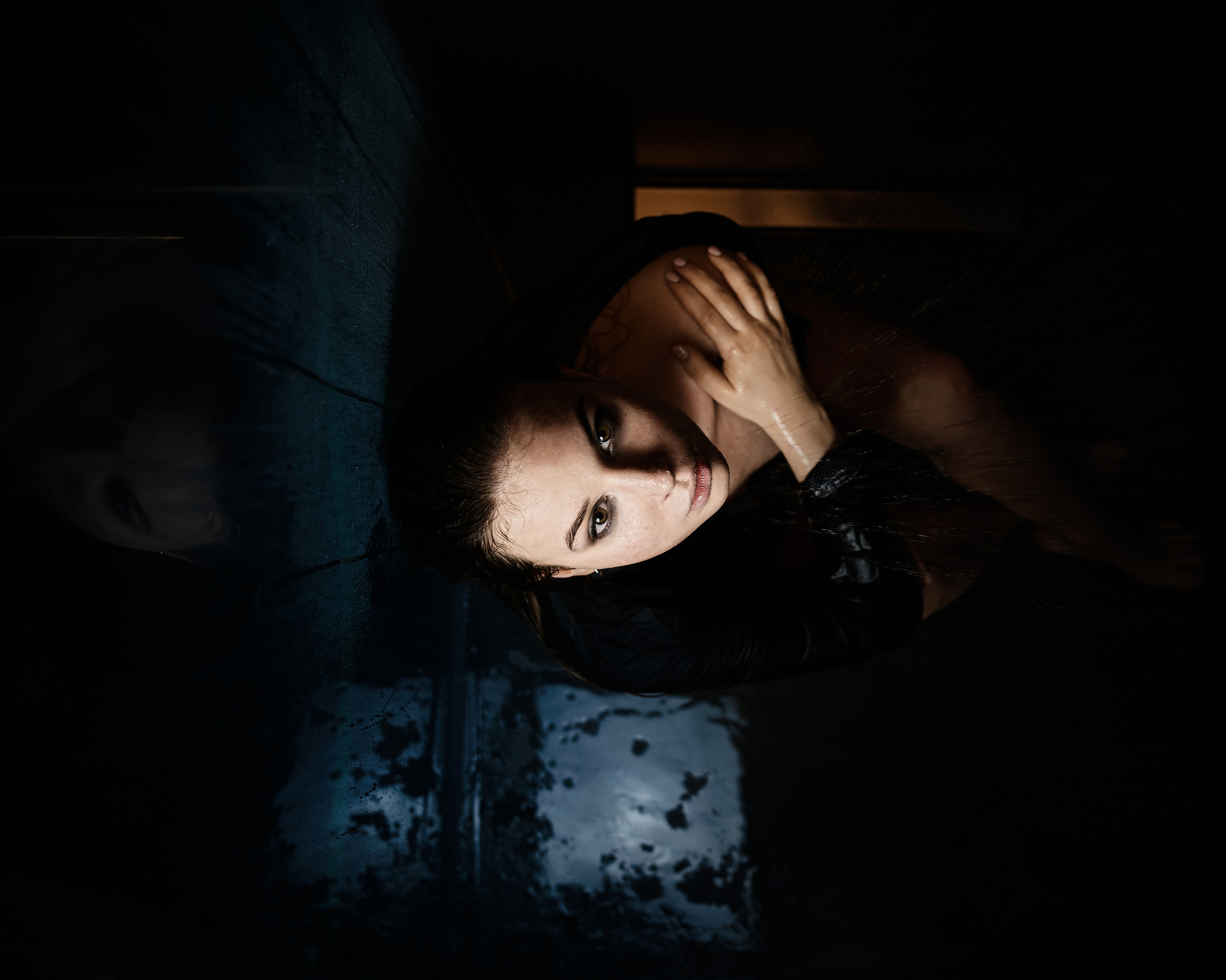 A contemplative woman shower lying beside a reflective surface, her face partially lit, creating a moody and artistic feel.