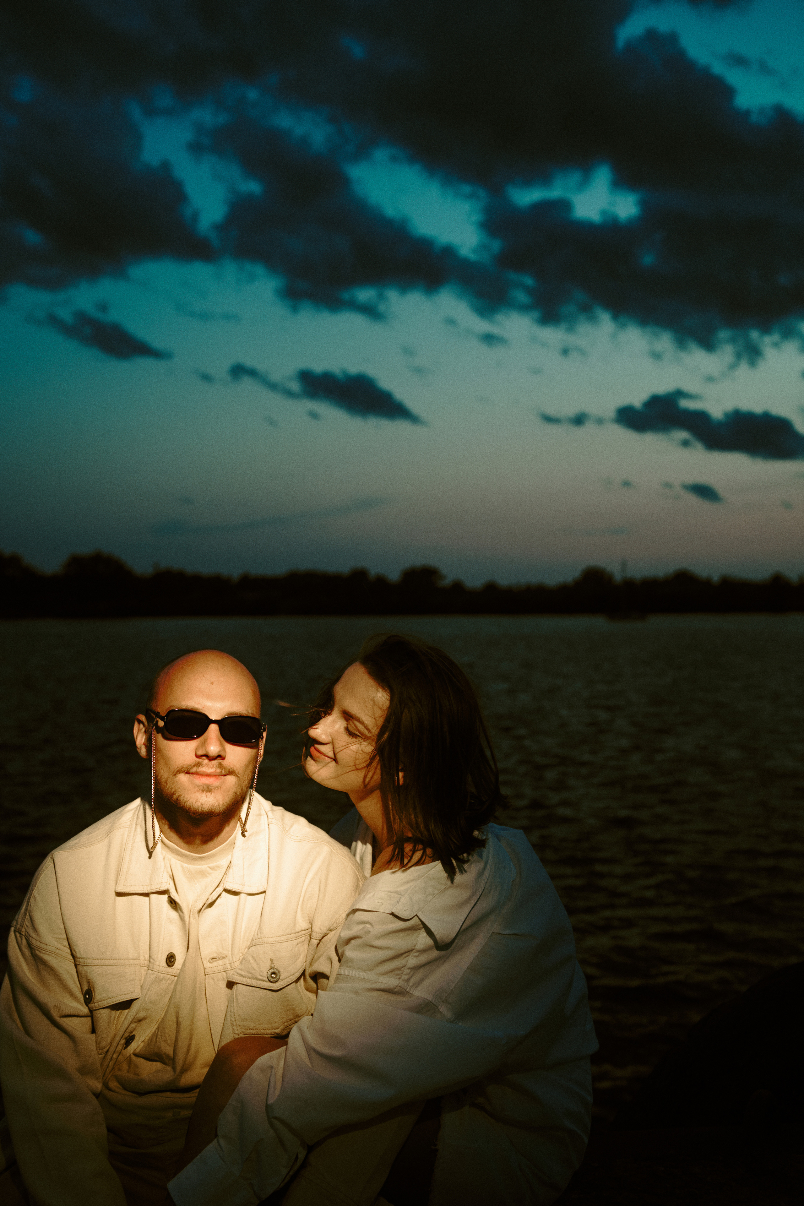 A couple enjoying an intimate moment by the water during twilight, framed by a serene and romantic setting.