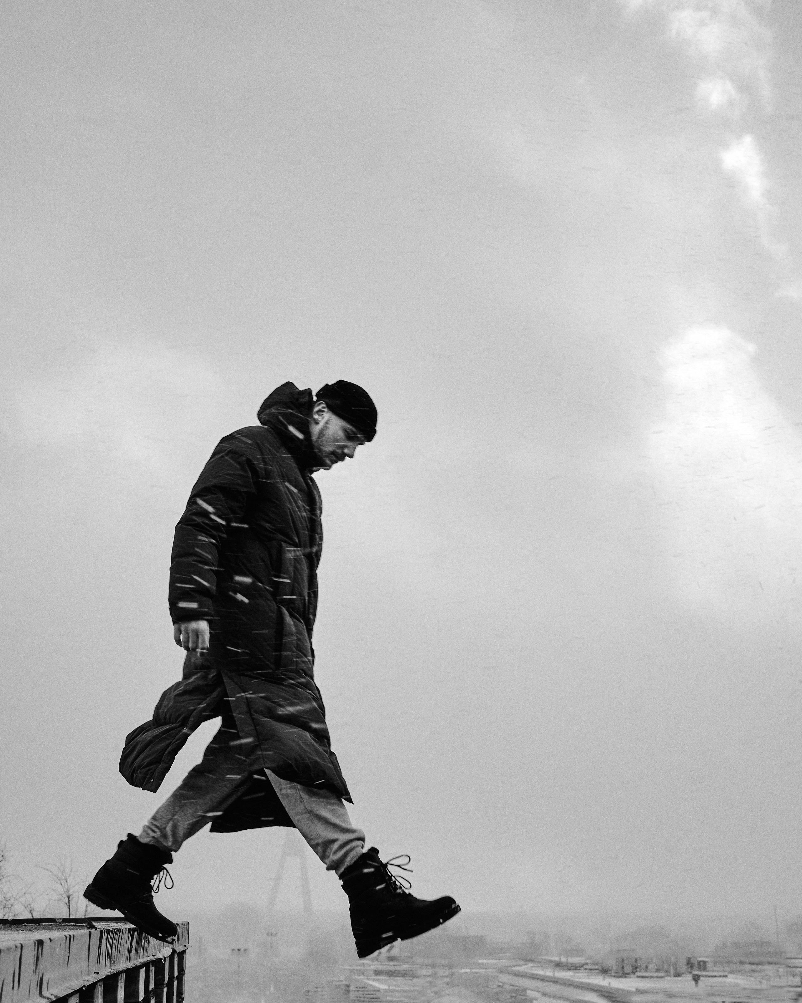  A black-and-white photo of a man walking on a foggy rooftop, creating a moody and cinematic atmosphere.