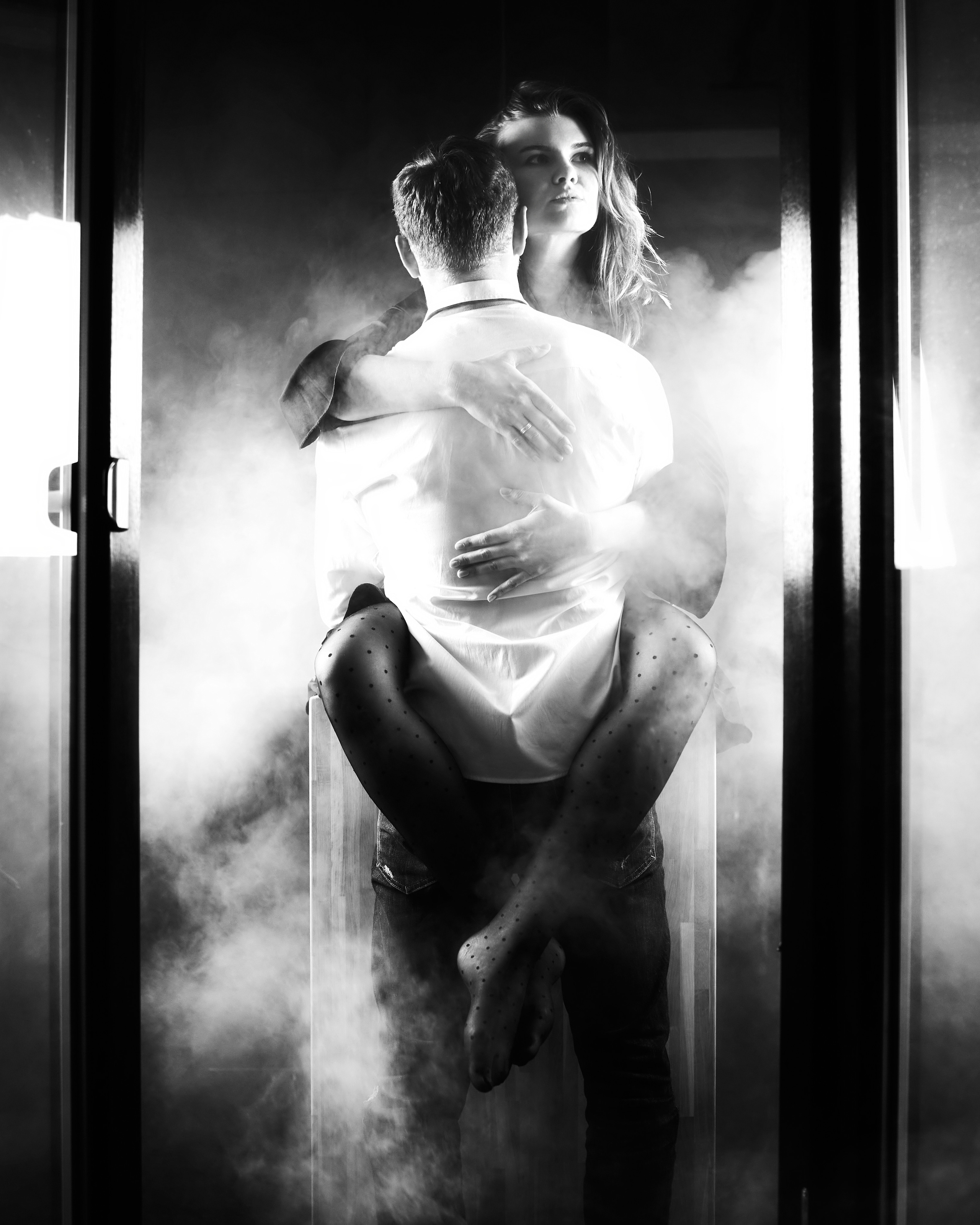 A couple passionately embracing in a smoky, backlit room, with dramatic lighting adding a sense of mystery.