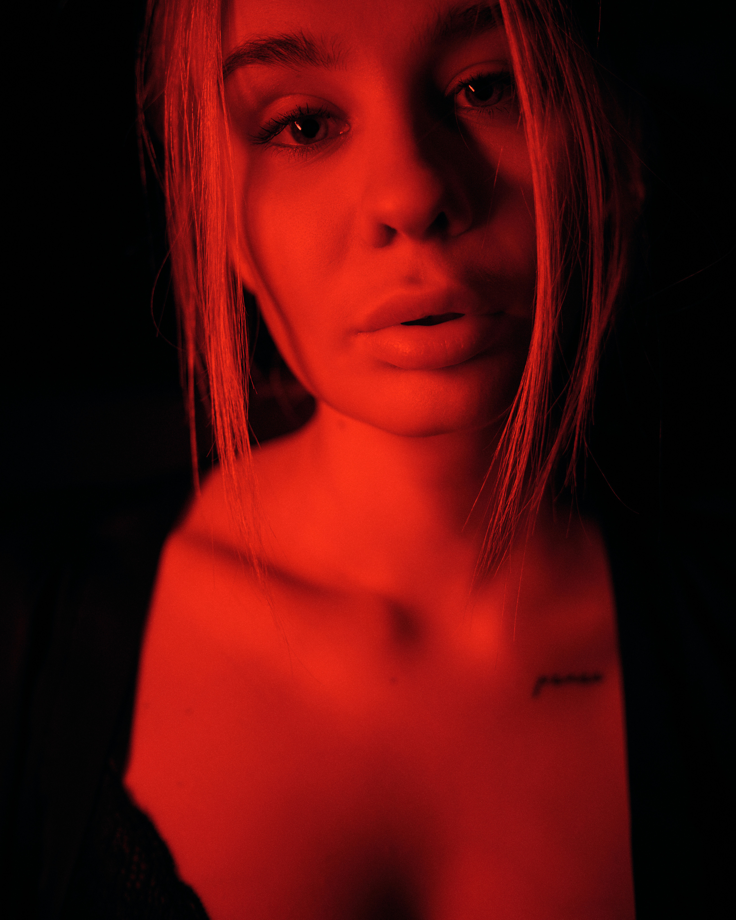 A red-lit close-up portrait of a woman with piercing eyes, creating a striking and bold visual impact.