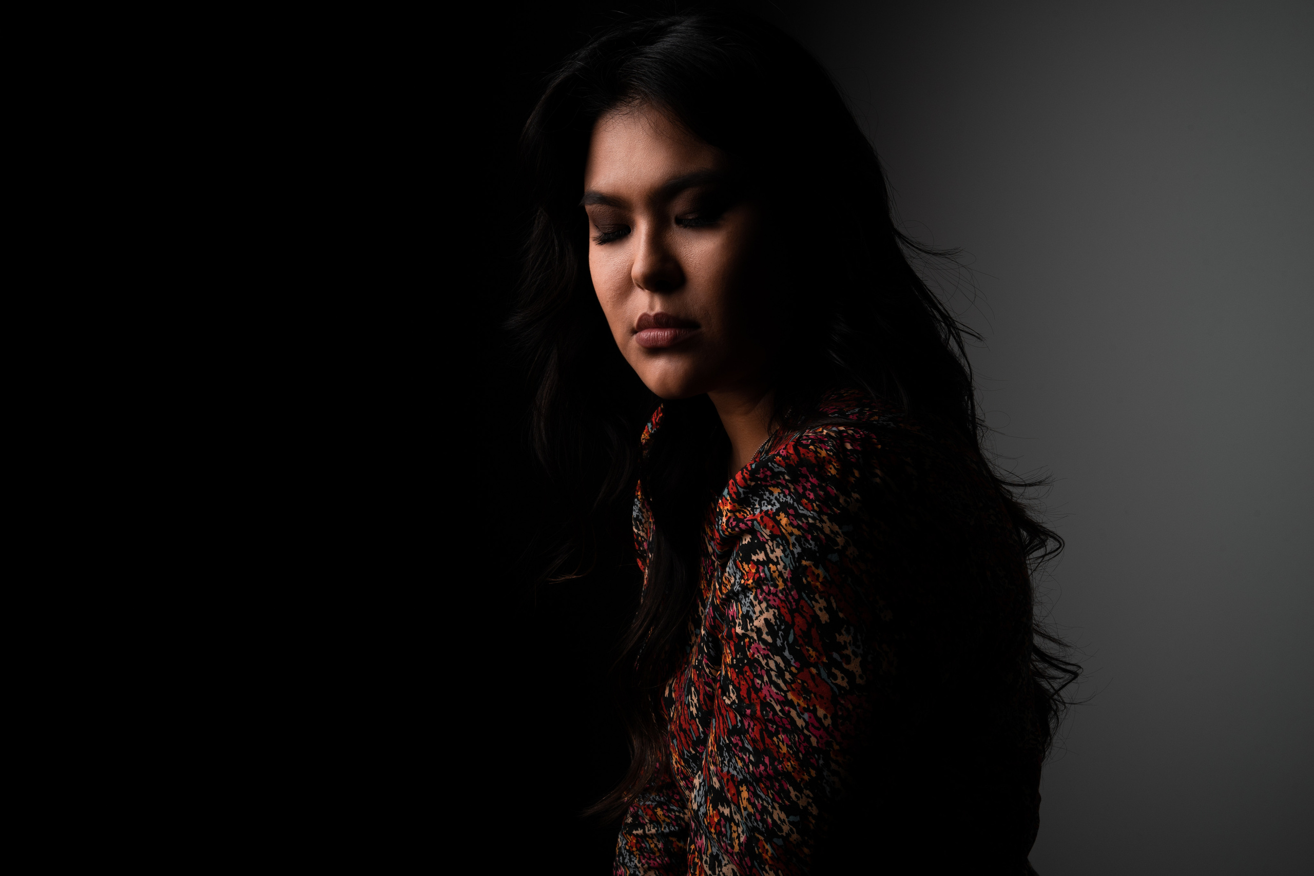 A studio portrait of a woman wearing a patterned jacket, with dramatic shadows highlighting her contemplative expression.