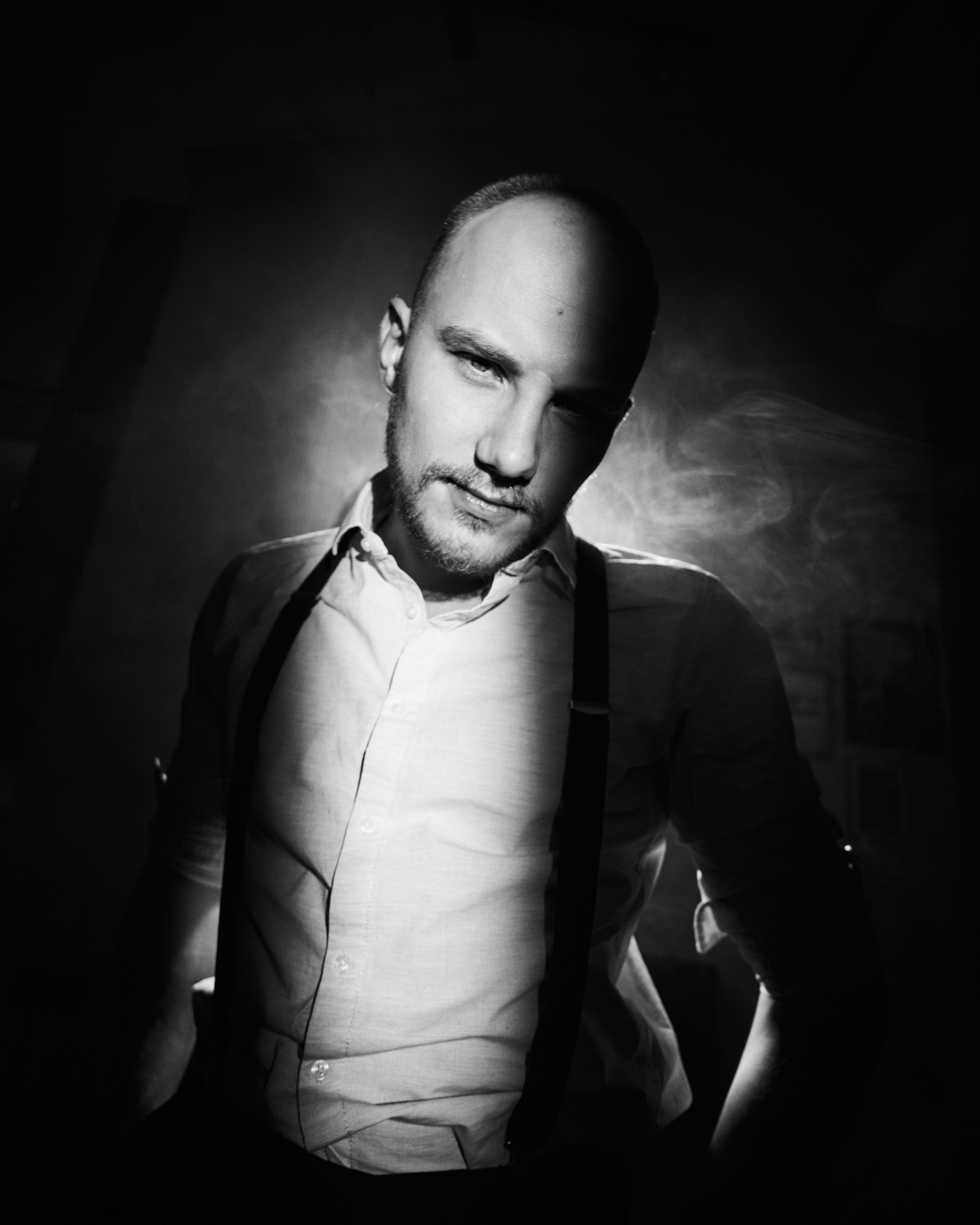  dramatic studio portrait of a bald man wearing suspenders, highlighted by directional lighting for a bold effect.