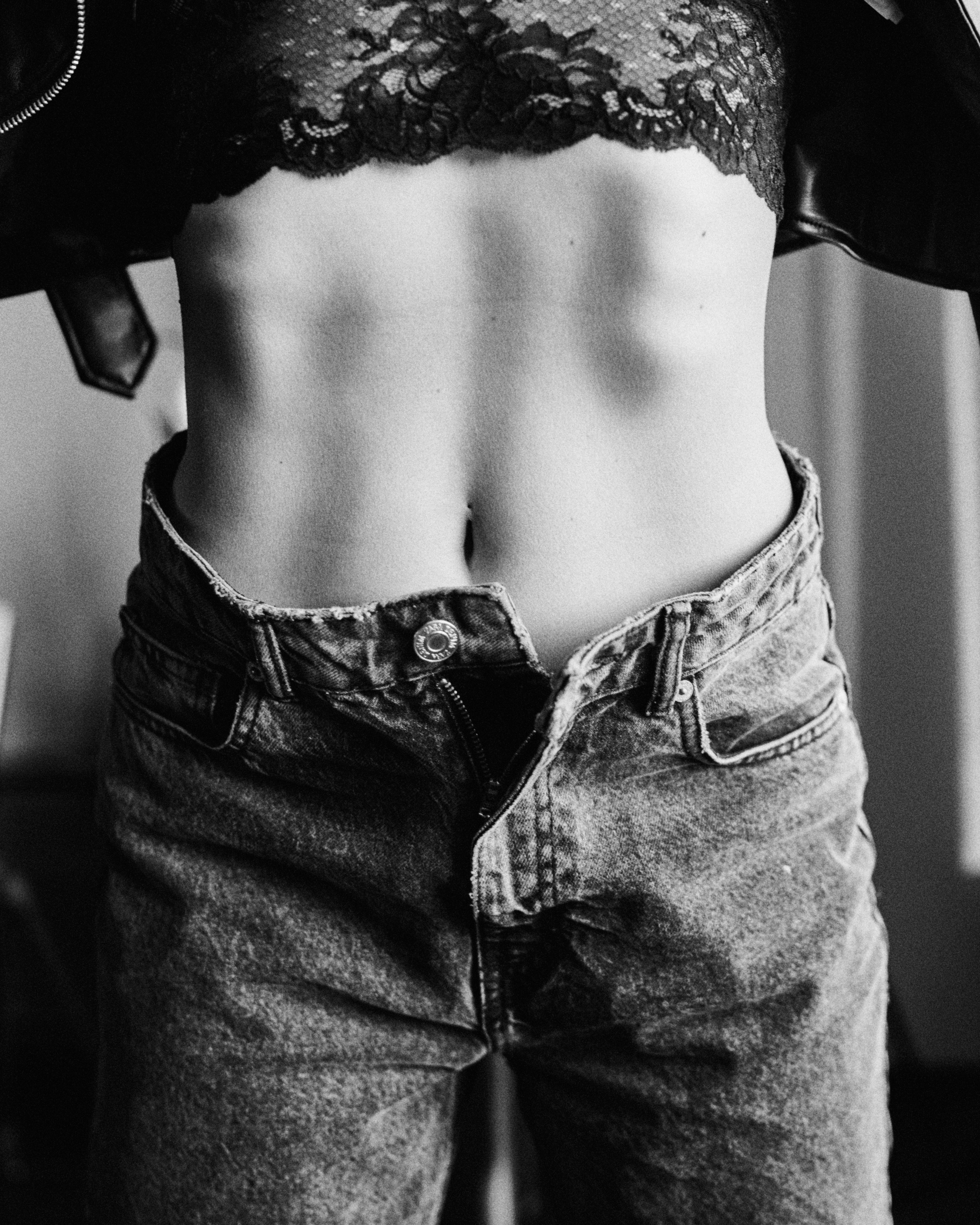 A black-and-white close-up of a person’s torso, showcasing defined abs, a lace bra, and high-waisted jeans.