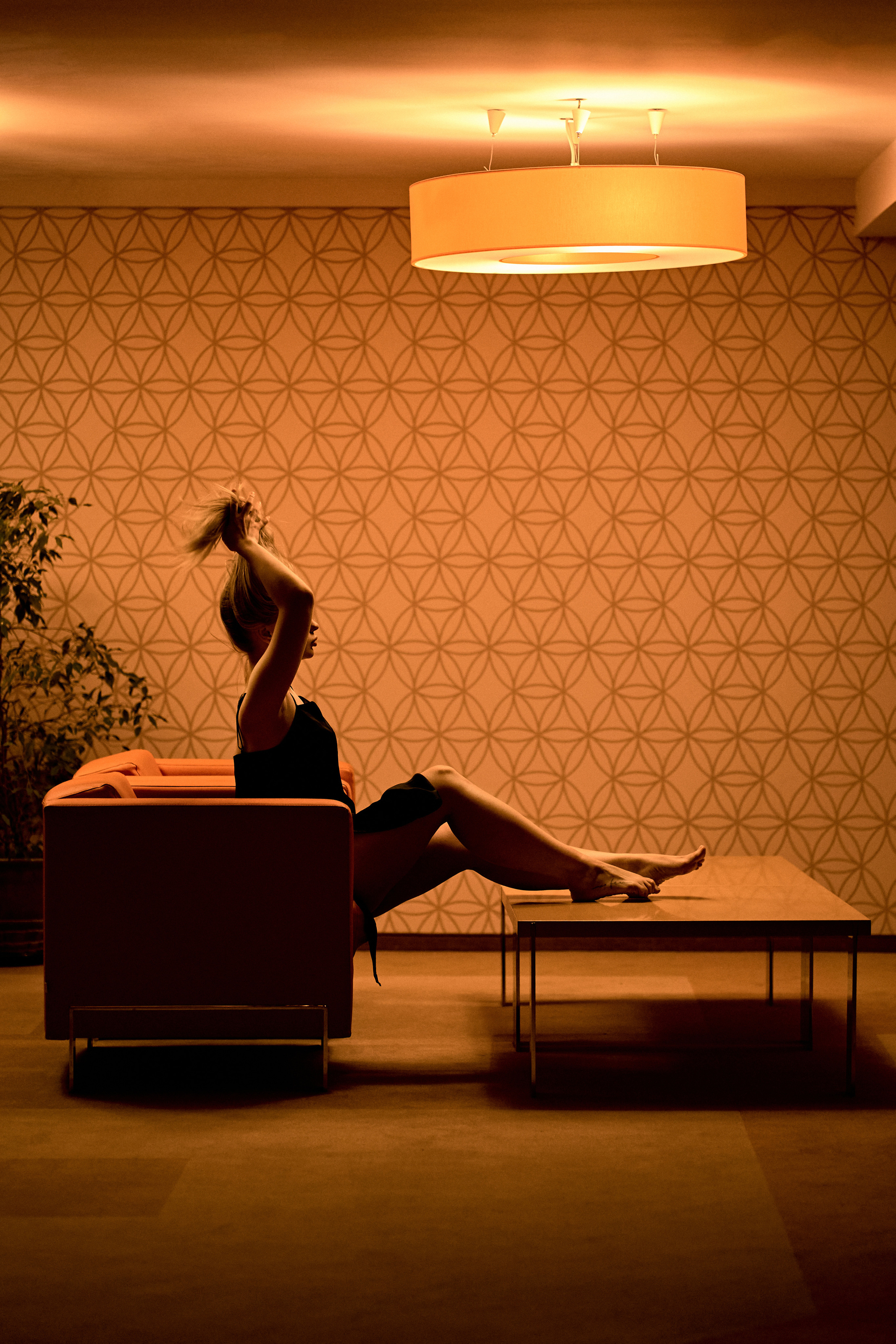  A silhouette of a woman in a retro-styled hotel lobby, lounging on a sofa under a warm ceiling light, evoking nostalgia.