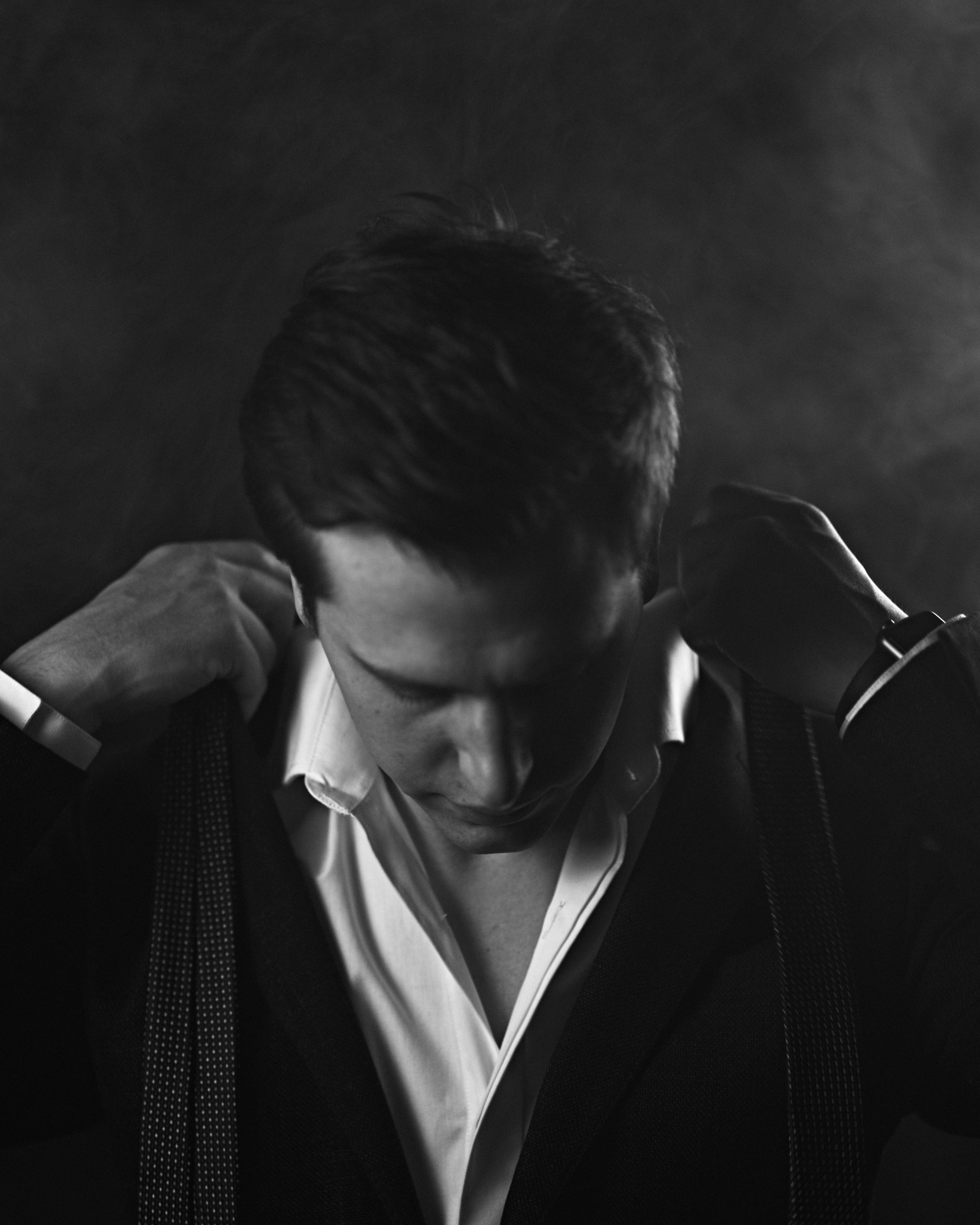 A black-and-white portrait of a man adjusting his blazer, with a focused and introspective expression.