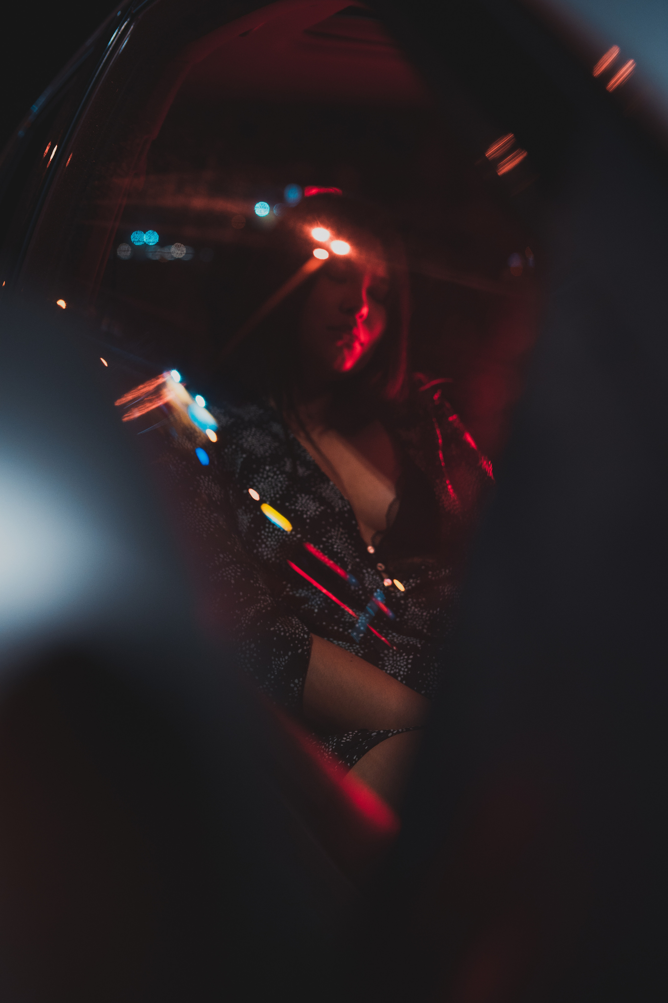 A woman in a dimly lit car, surrounded by red and yellow lights, creating a moody and cinematic atmosphere.