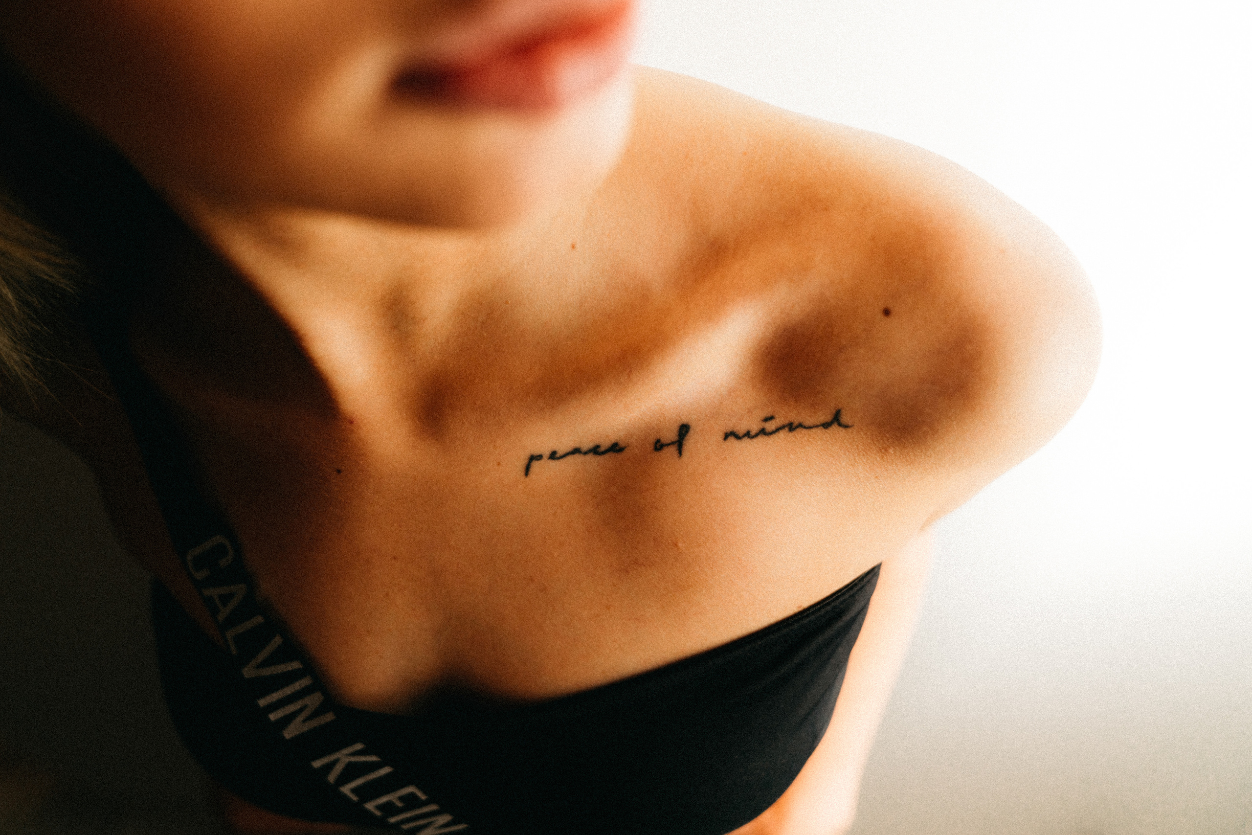 A close-up of a woman’s collarbone and tattoo, with soft lighting enhancing the minimalistic and intimate mood.