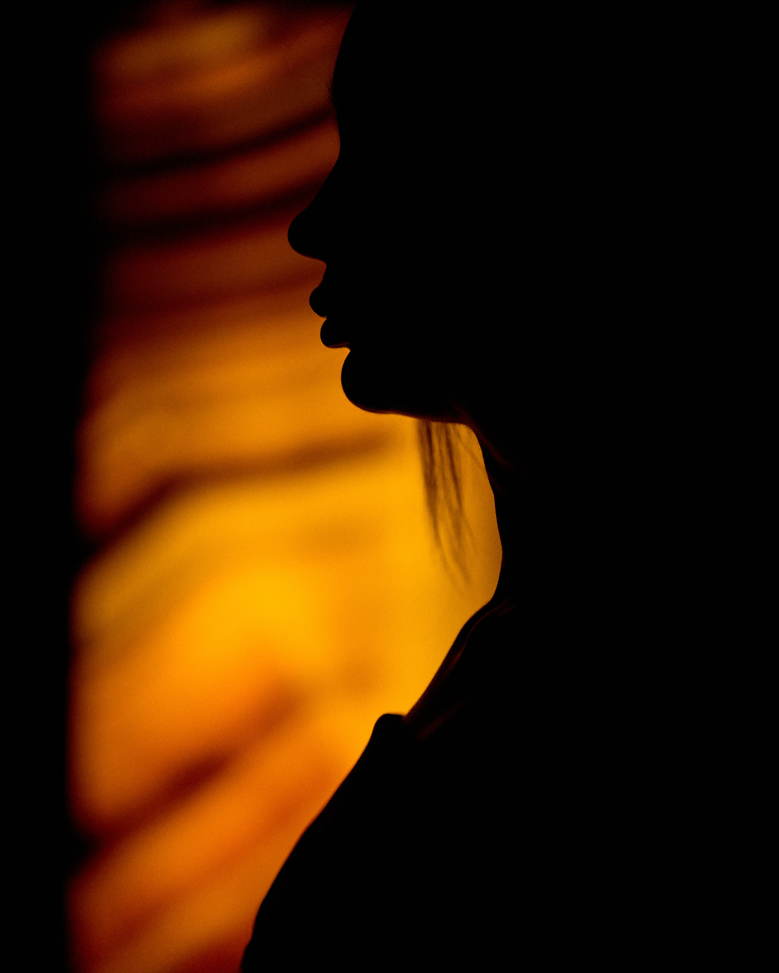 A silhouette of a woman against a glowing orange backdrop, creating a dramatic and abstract visual.