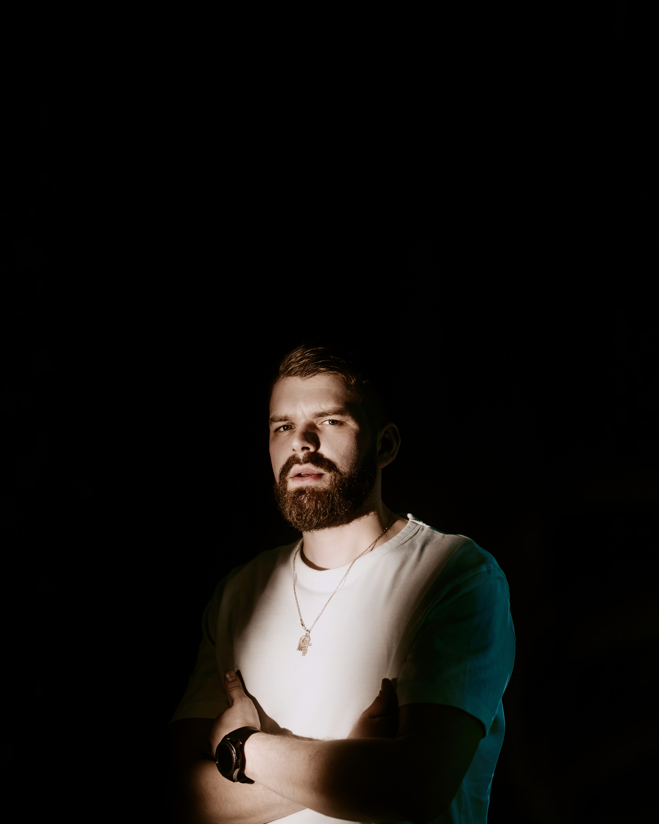 A low-key portrait of a man wearing a white T-shirt, his face illuminated against a dark backdrop.