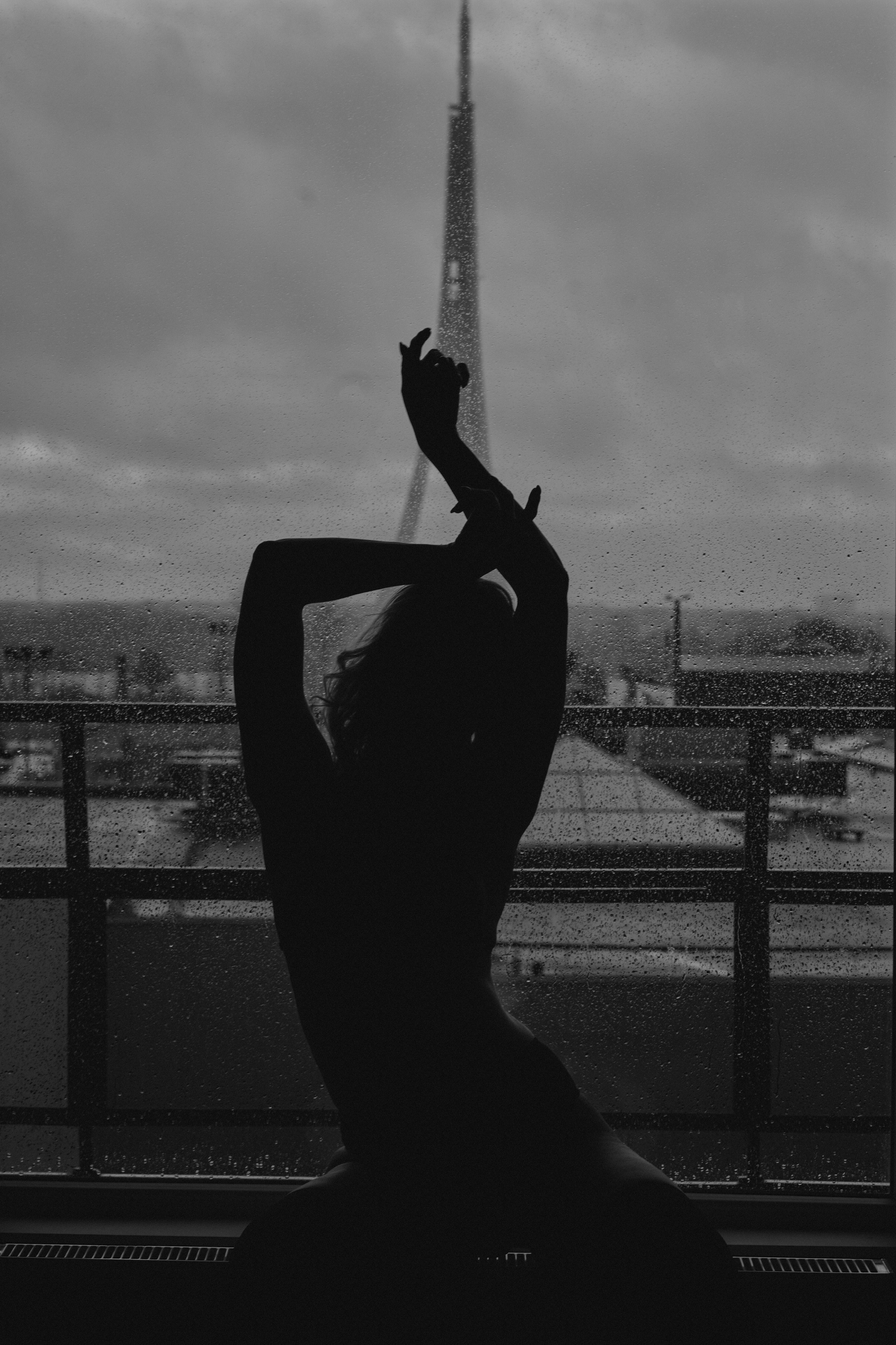 A silhouetted figure of a woman performing an elegant pose on a pole with an urban skyline in the background.