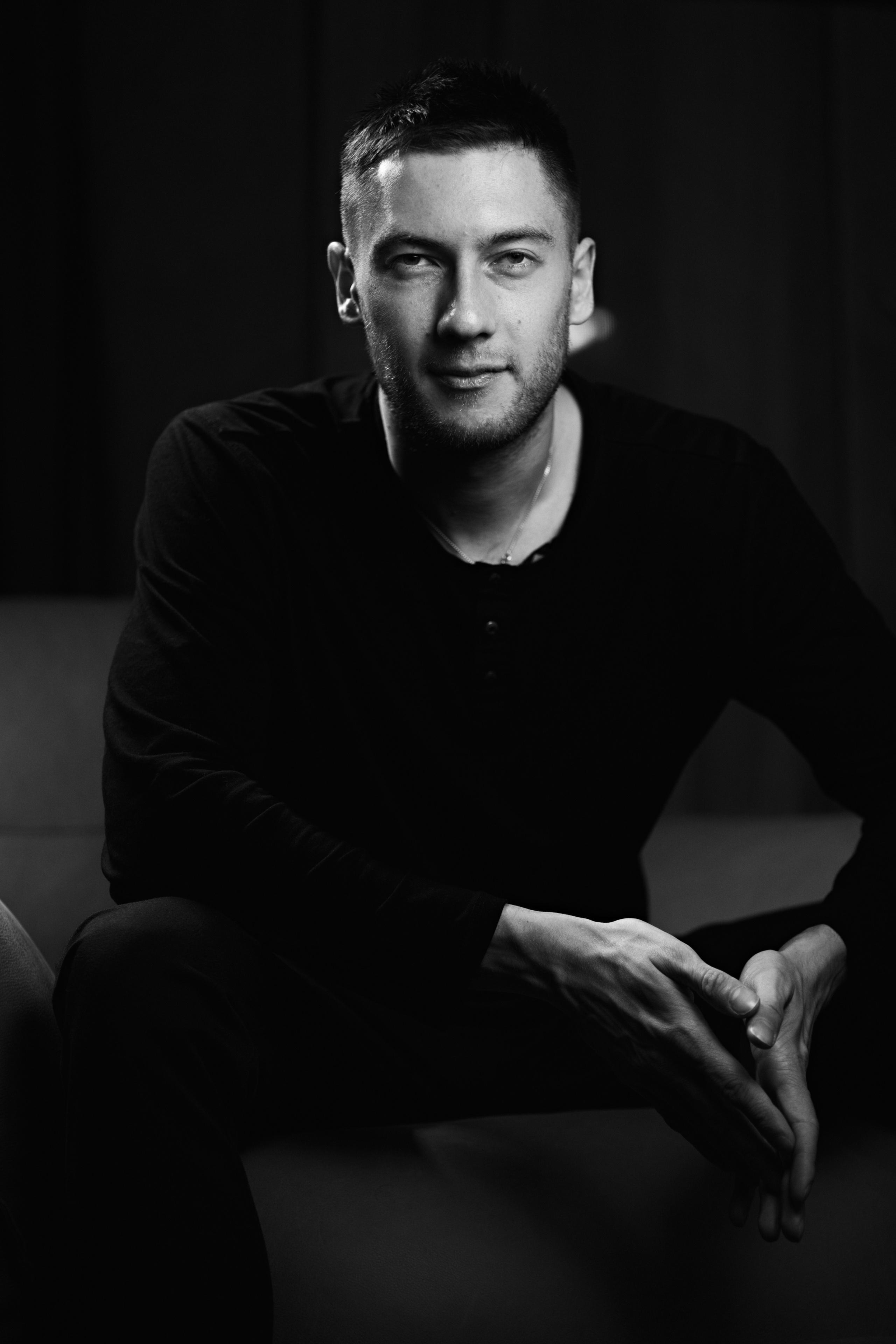  formal portrait of a man sitting with a calm and confident expression in a minimalist setting.