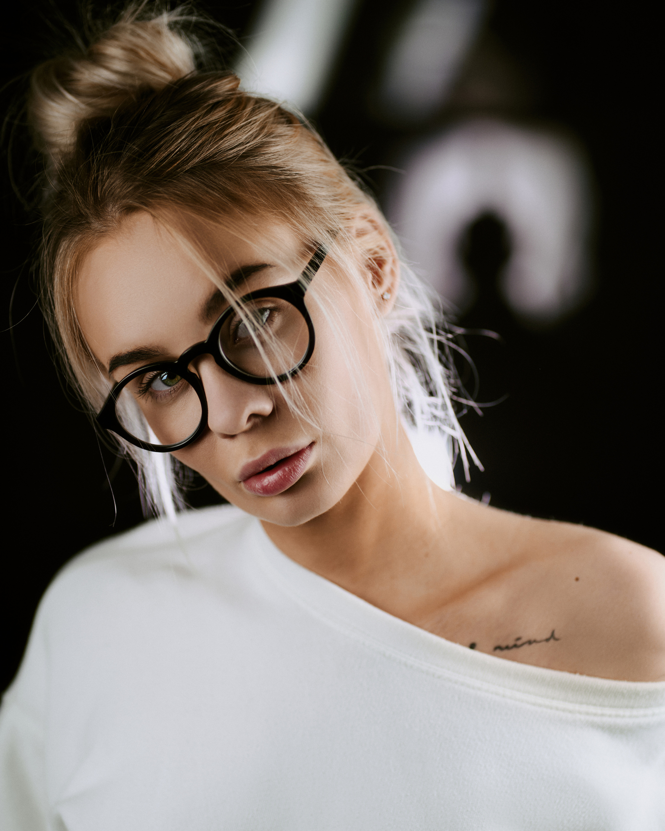 A portrait of a woman wearing oversized glasses and a white sweater, captured in soft and intimate lighting.