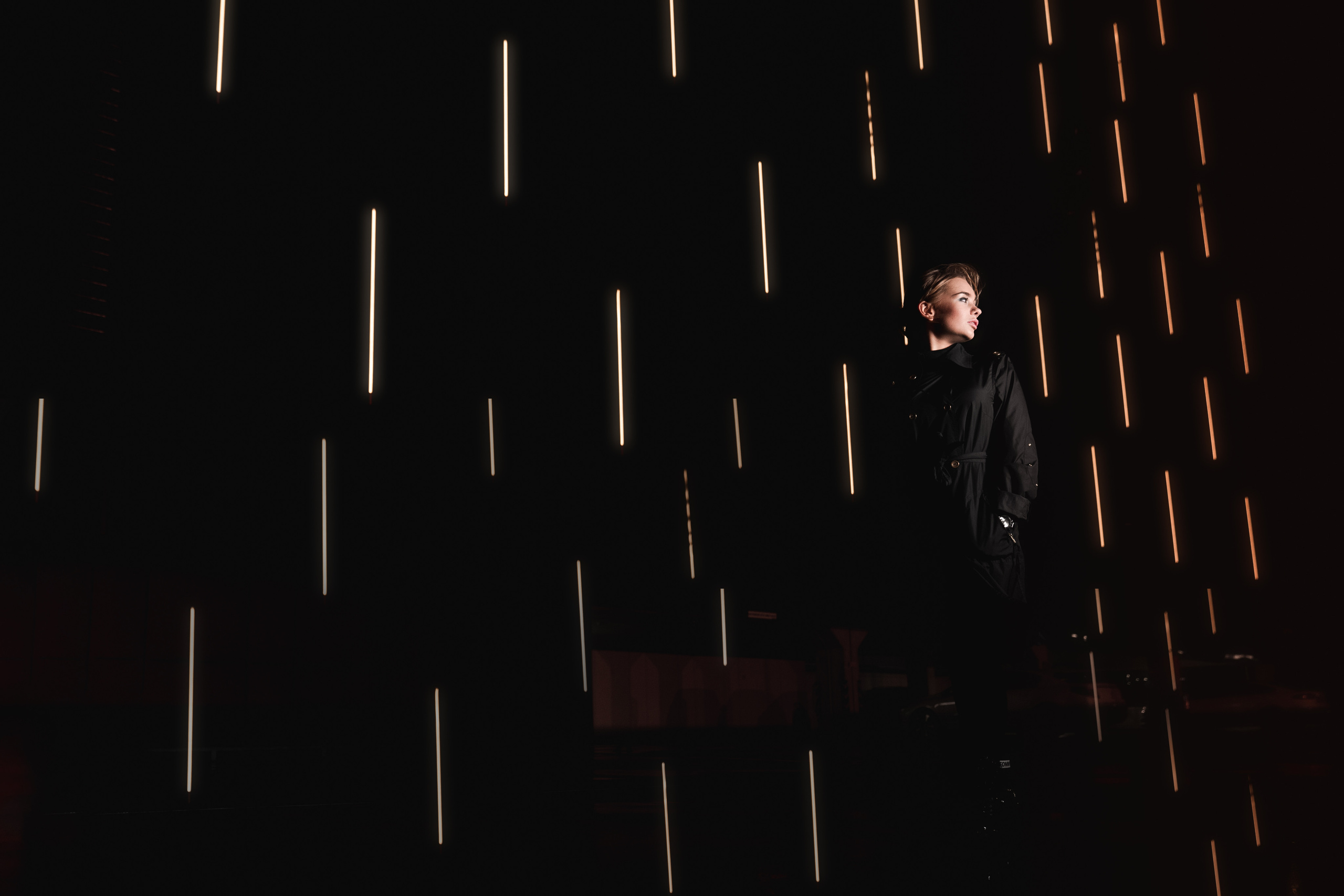 A minimalist photo of a dark space with streaks of light illuminating a single figure in a suit, evoking mystery and sophistication.