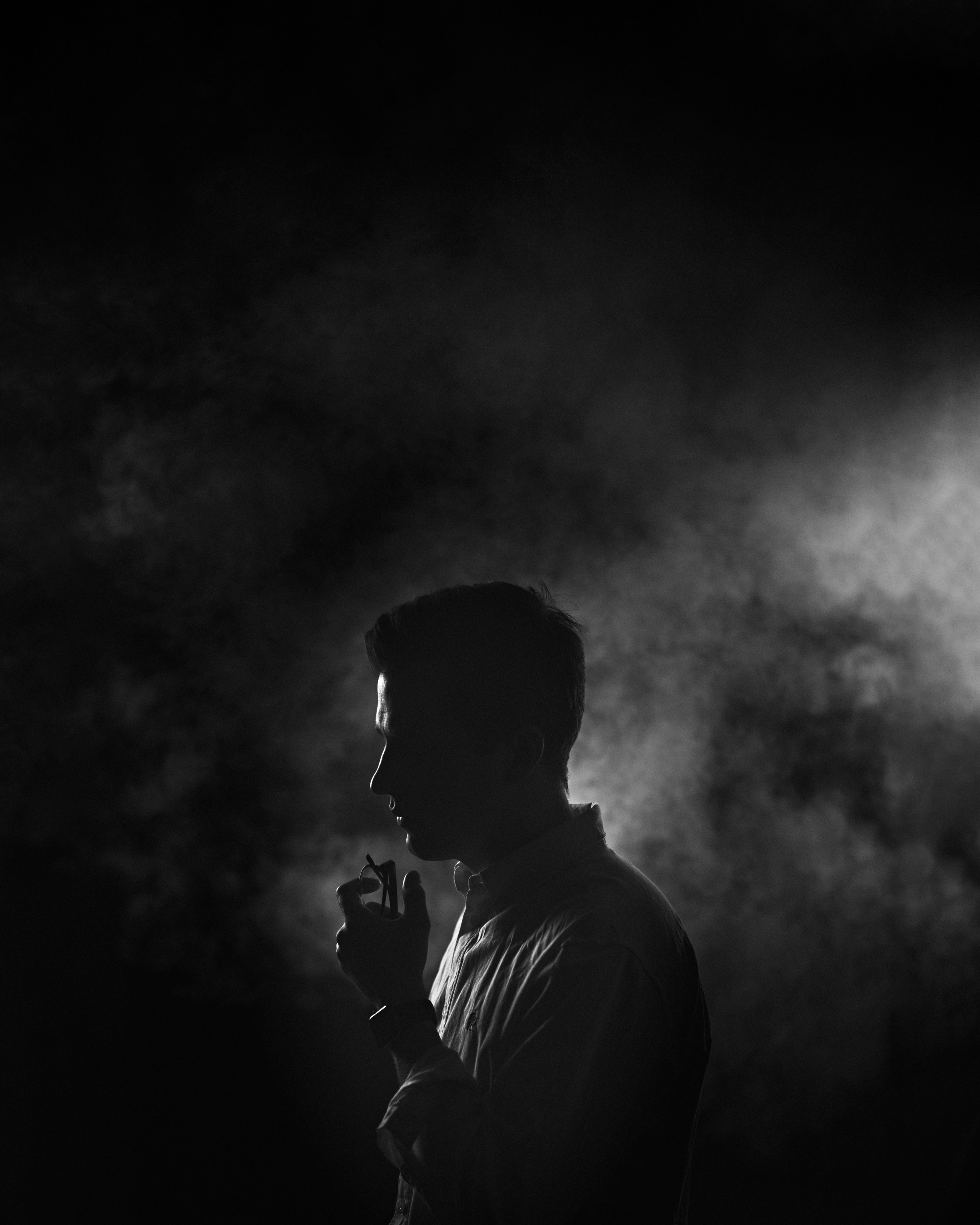 A dramatic side profile of a man surrounded by smoke, illuminated by soft lighting, creating a mysterious and introspective tone.