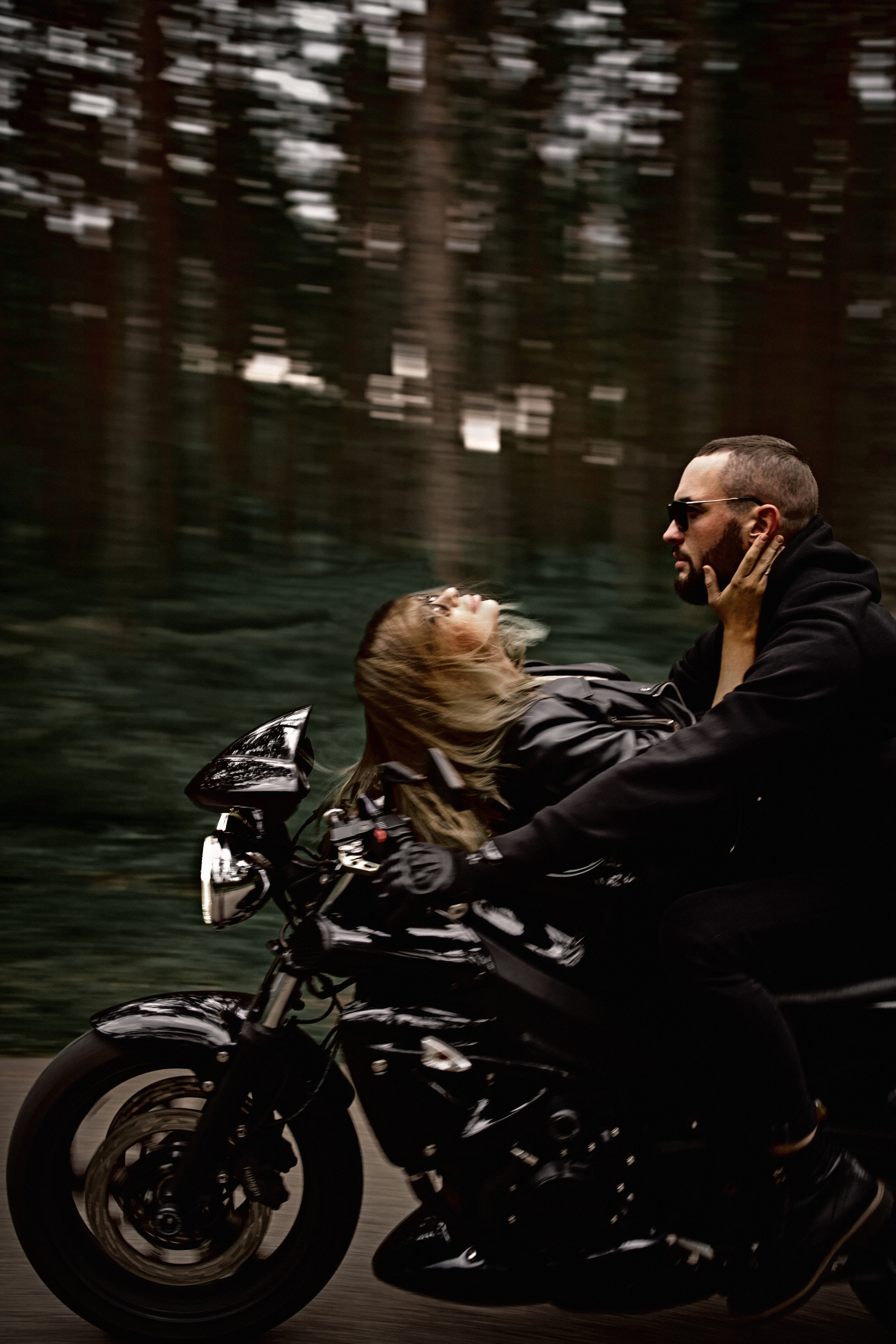 A couple riding a motorcycle through a blurred forested background, showcasing motion and freedom.