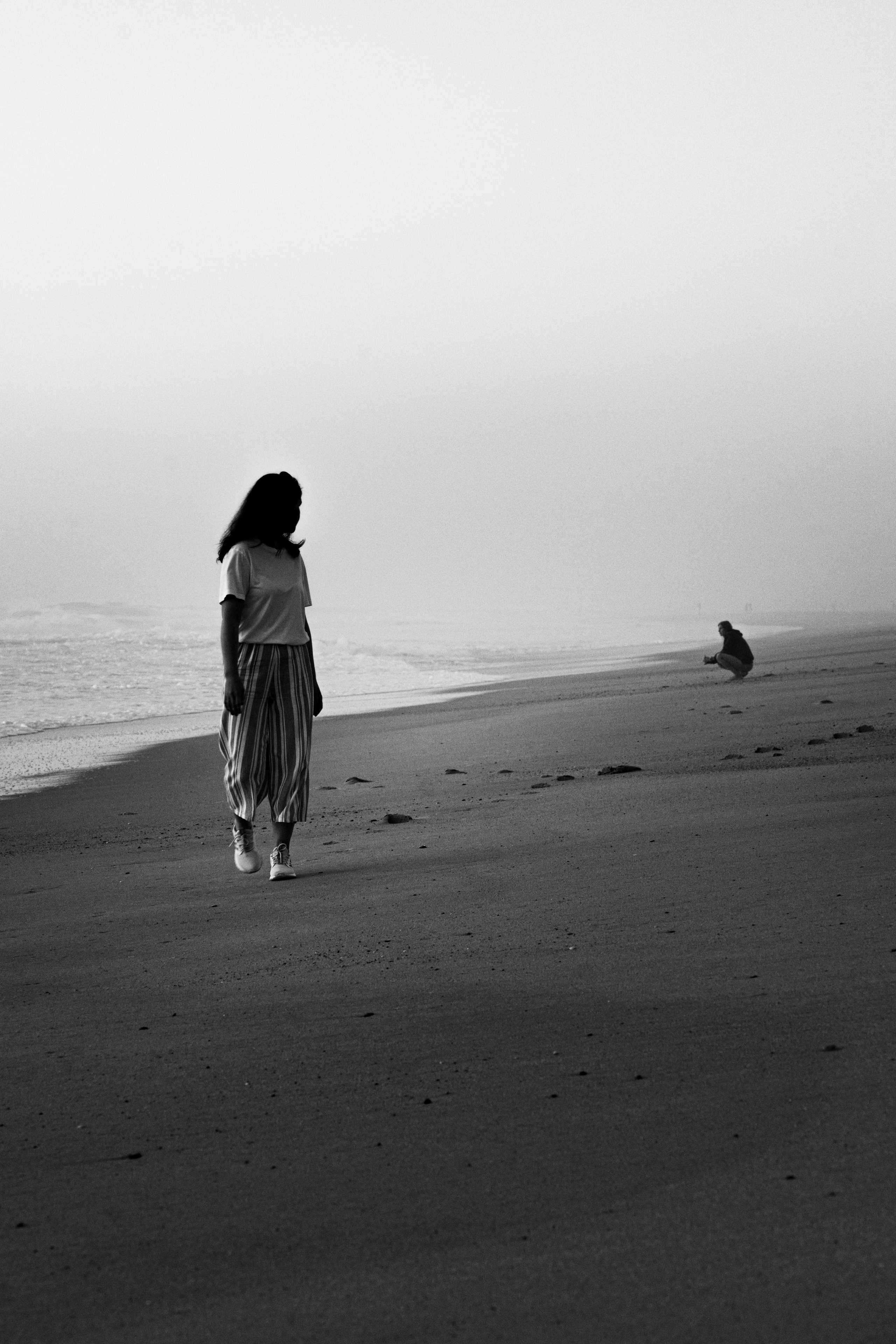 A contemplative shot of a woman standing alone on a beach, looking out to the horizon, with soft, muted tones.