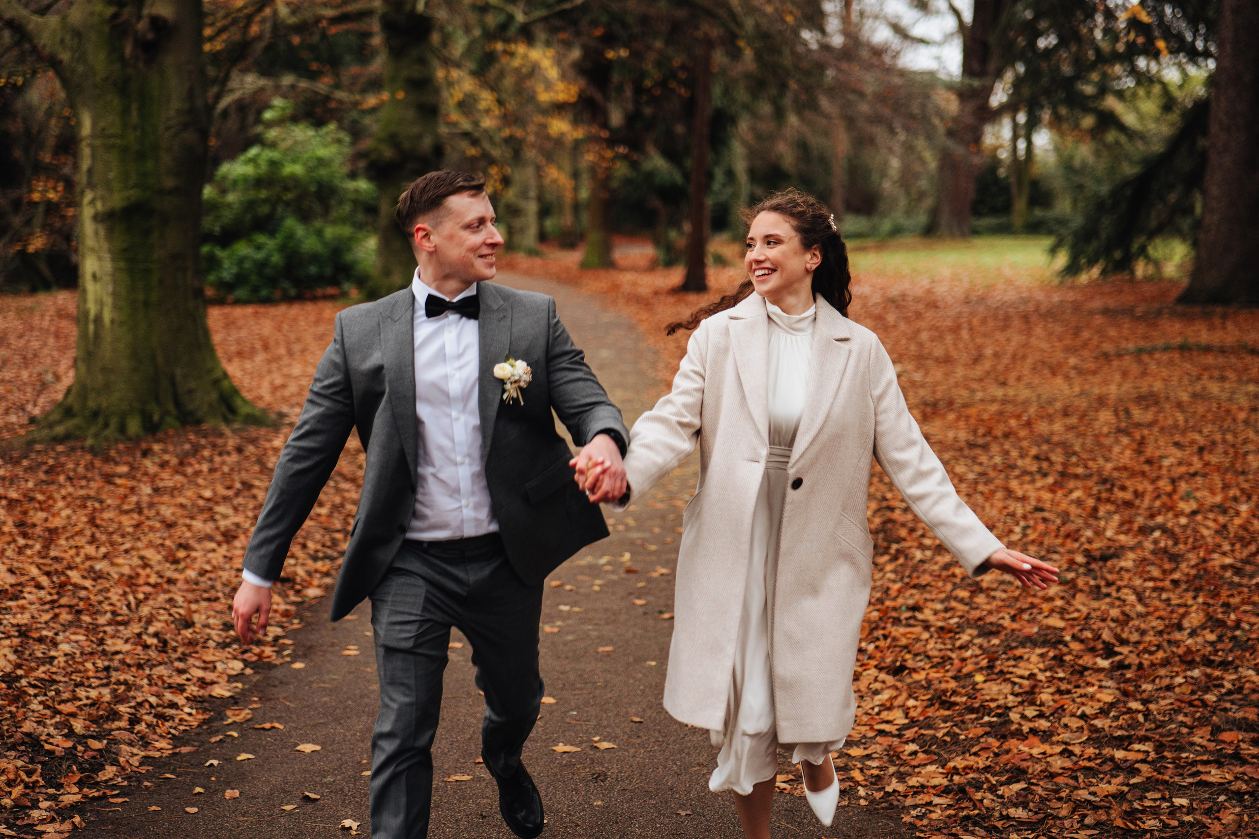 bride and groom running while holding hands in autumn park