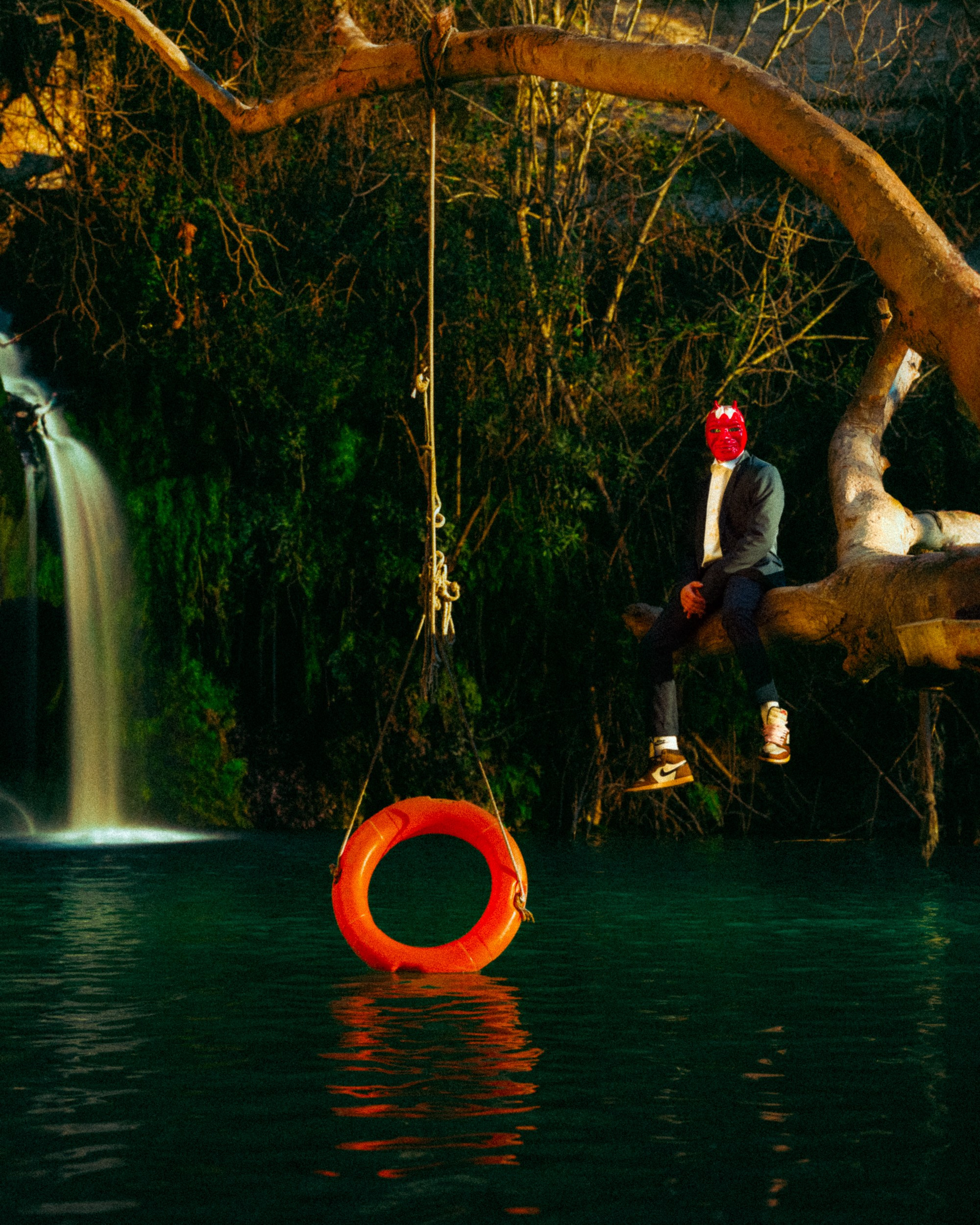 A man sitting on a tree over a lake with a red mask on his face 