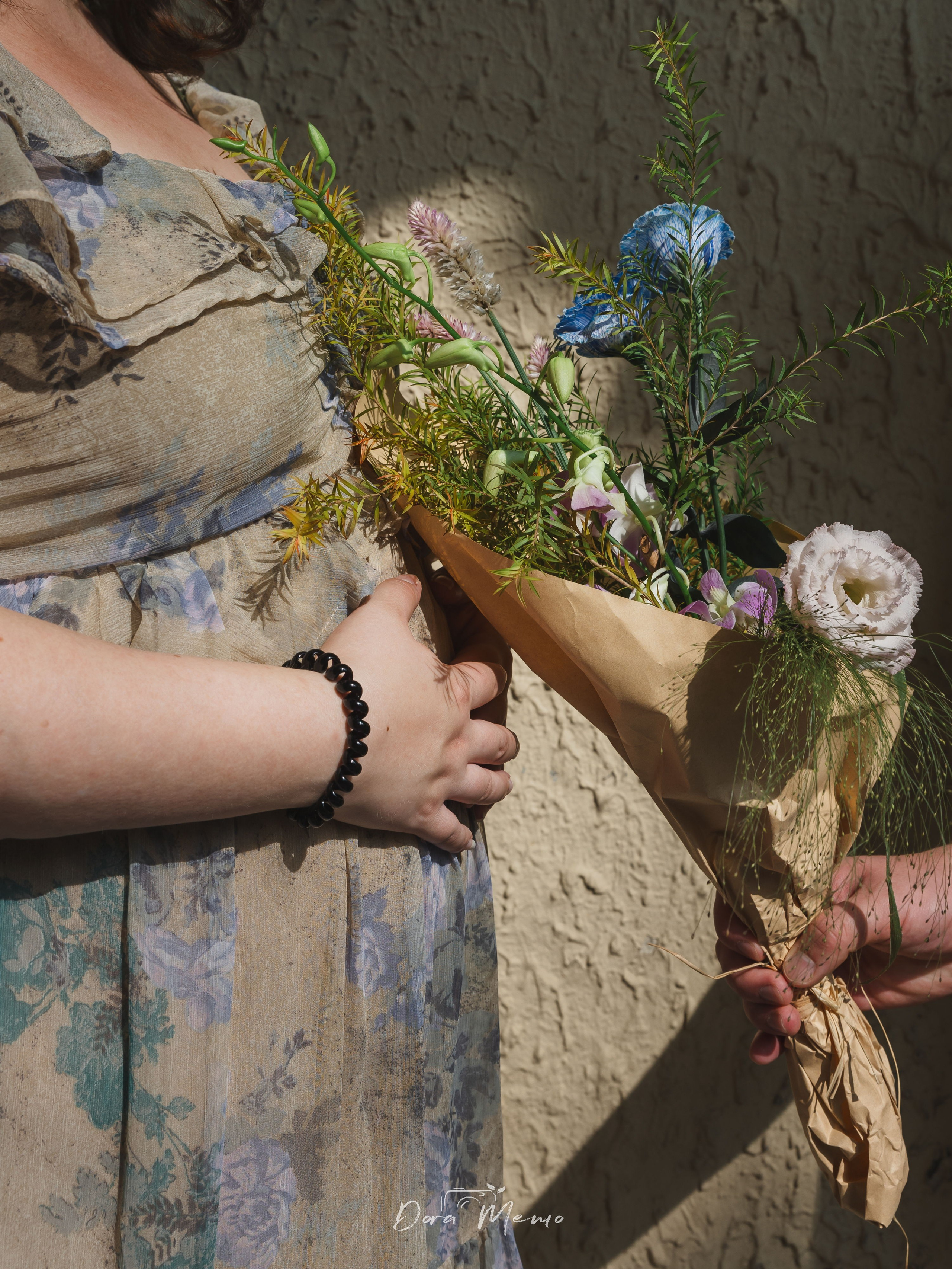  A quiet detail photograph of a pregnant belly, hands, and flowers in warm natural light.