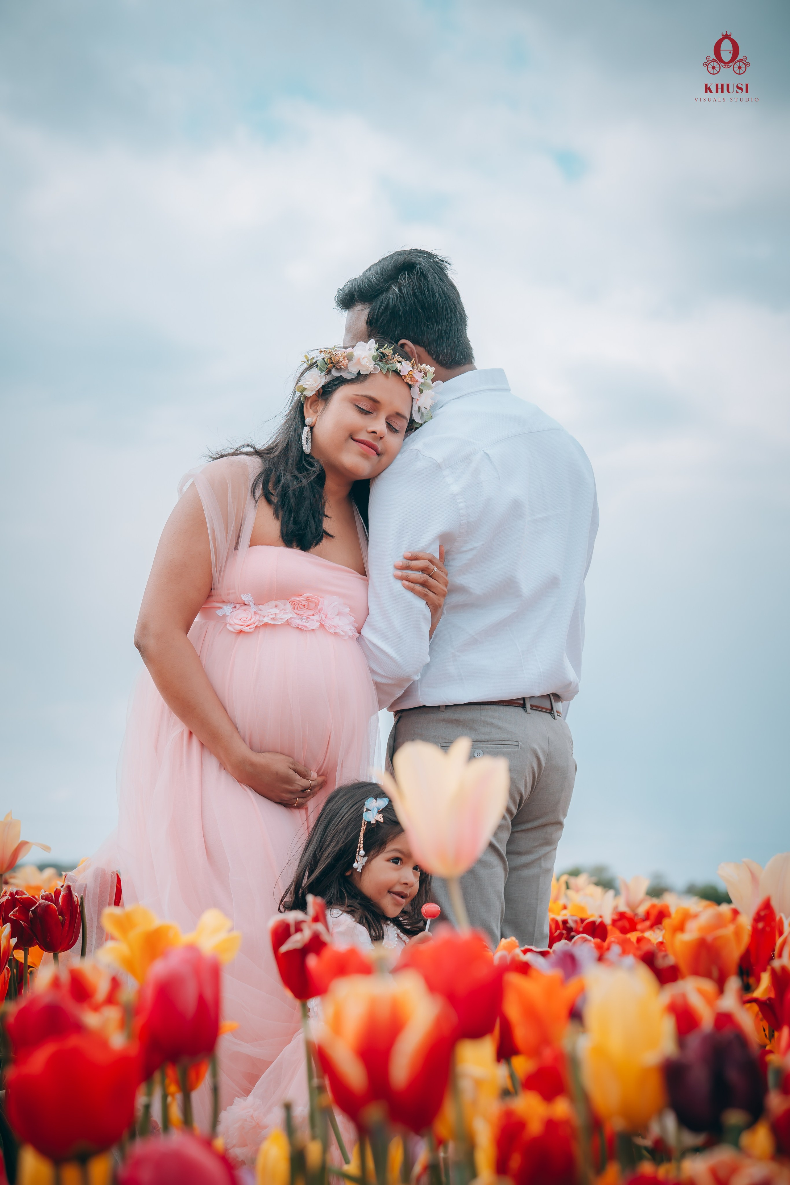 a pregnant couple with their daughter leaning on each other and their daughter playing with tulip flowers in Netherlands