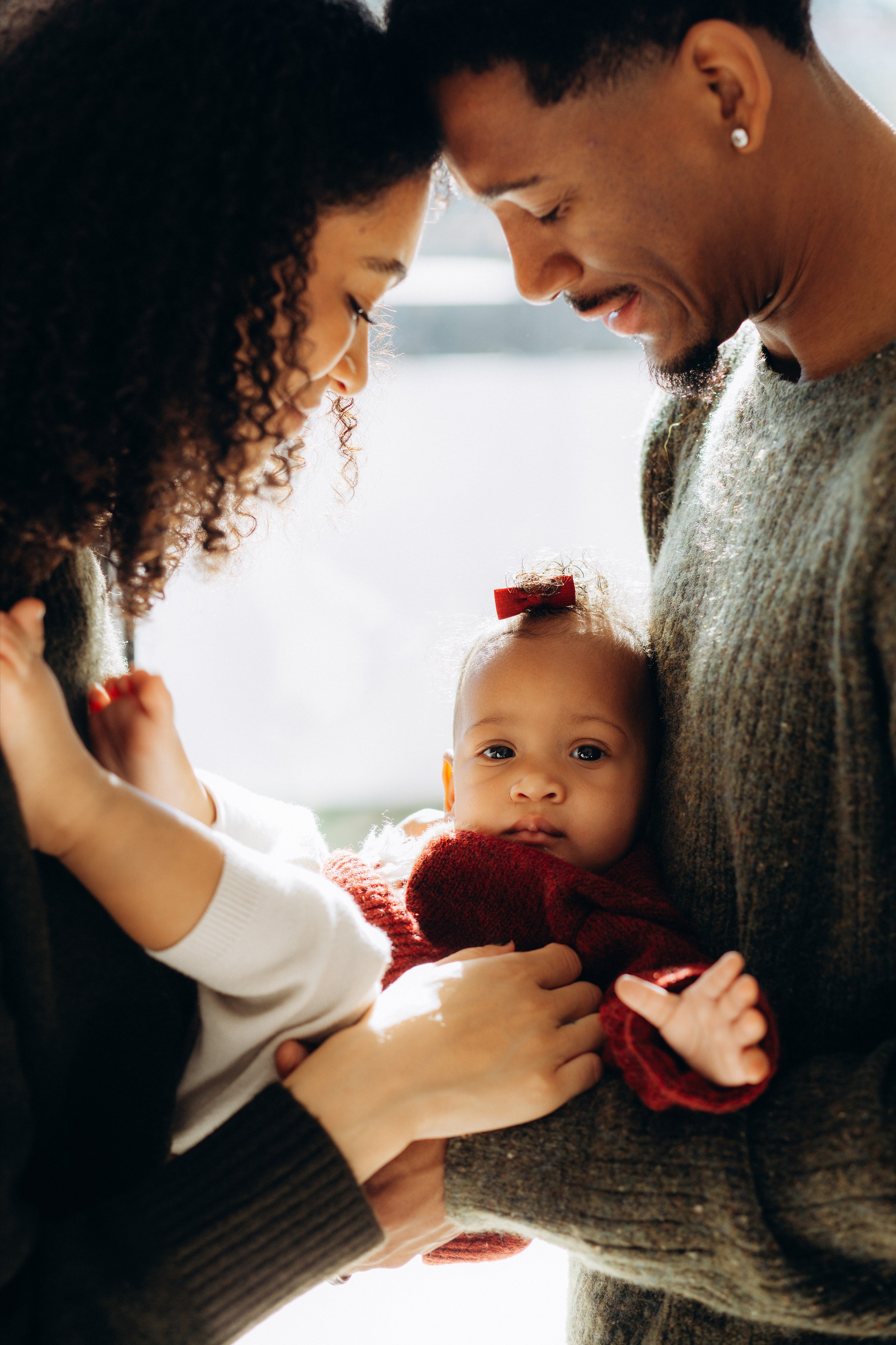 Sesión de fotos familiar en València, España, que captura un momento tierno e íntimo de unos padres amorosos sosteniendo a su bebé con cariño, fotografiado con luz natural suave, una conexión emocional cálida y expresiones auténticas, resaltando la maternidad, el vínculo y el amor familiar — ideal para fotografía familiar, sesiones de recién nacidos y bebés, retratos familiares lifestyle y sesiones familiares emotivas en València y en toda España.