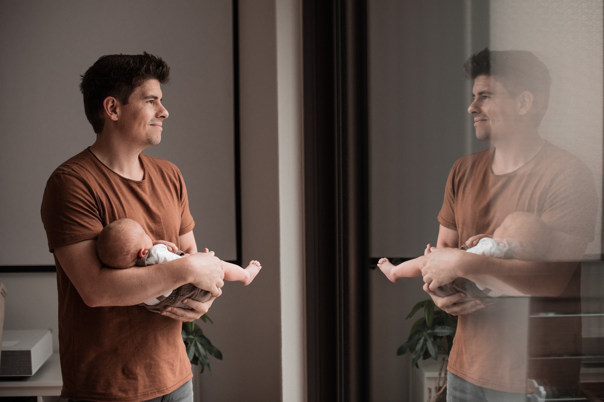 Vater steht mit seinem Sohn auf dem Arm und schaut aus dem Fenster in die Ferne.