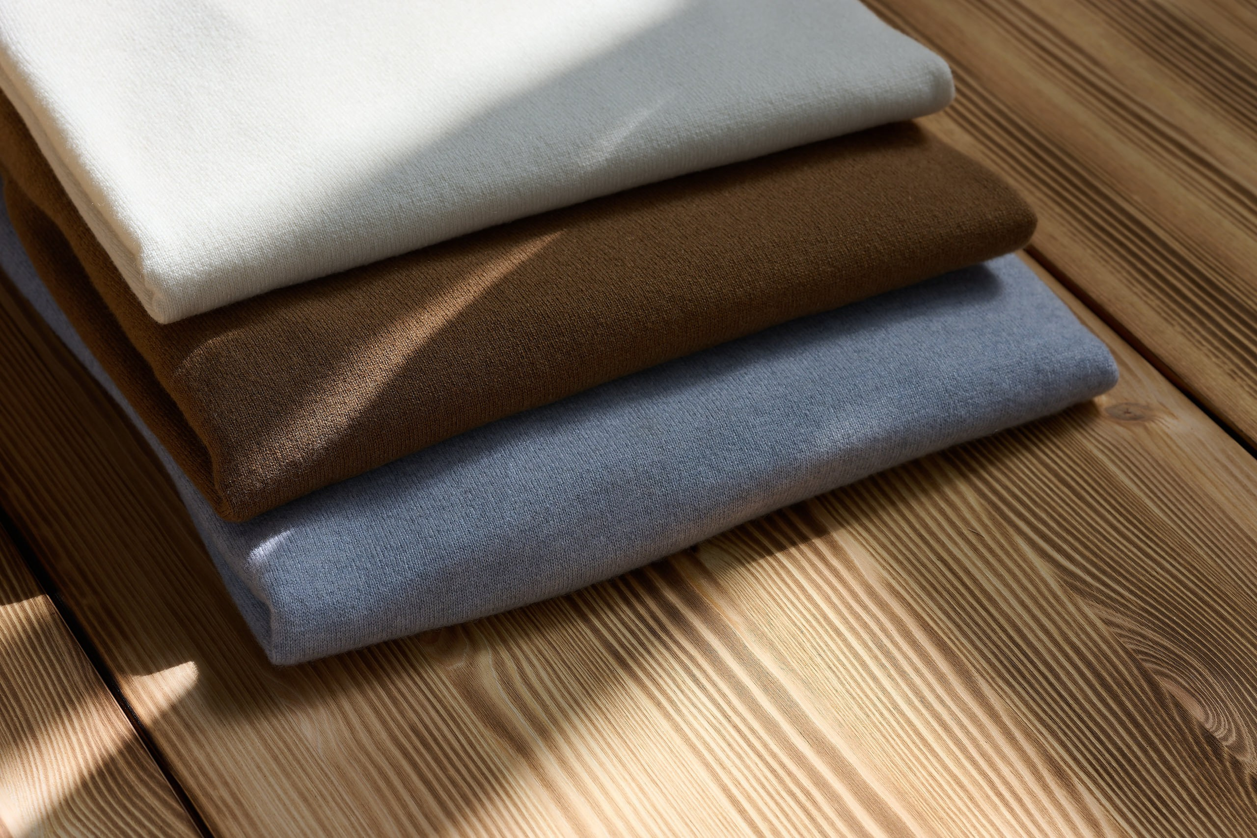 Produktfotografie Wien – Stapel aus gefalteten Stoffen in neutralen Farbtönen auf Holztisch.