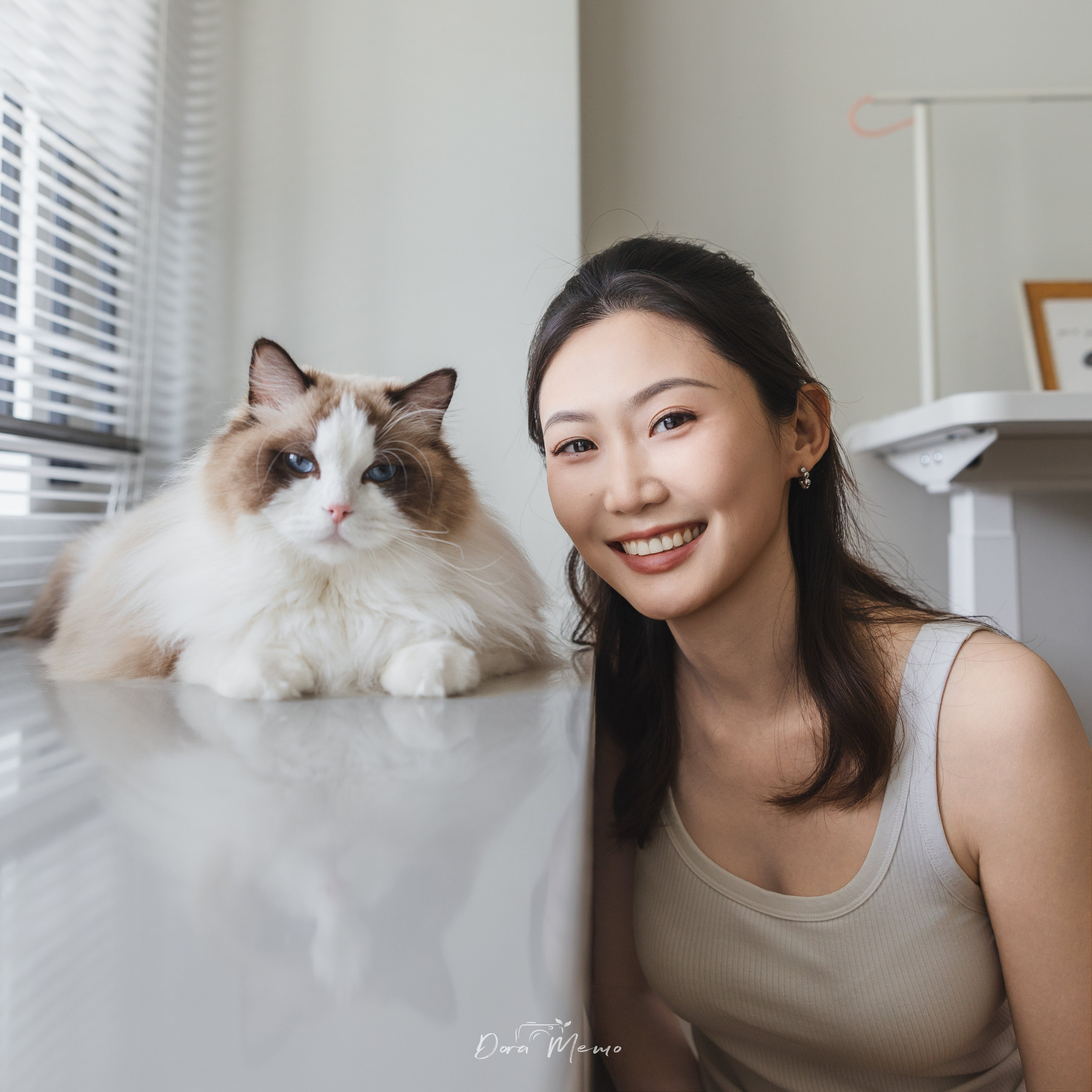 A young woman smiles next to her ragdoll cat on a windowsill, both gazing toward the camera — photographed by a Shanghai family and pet photographer.