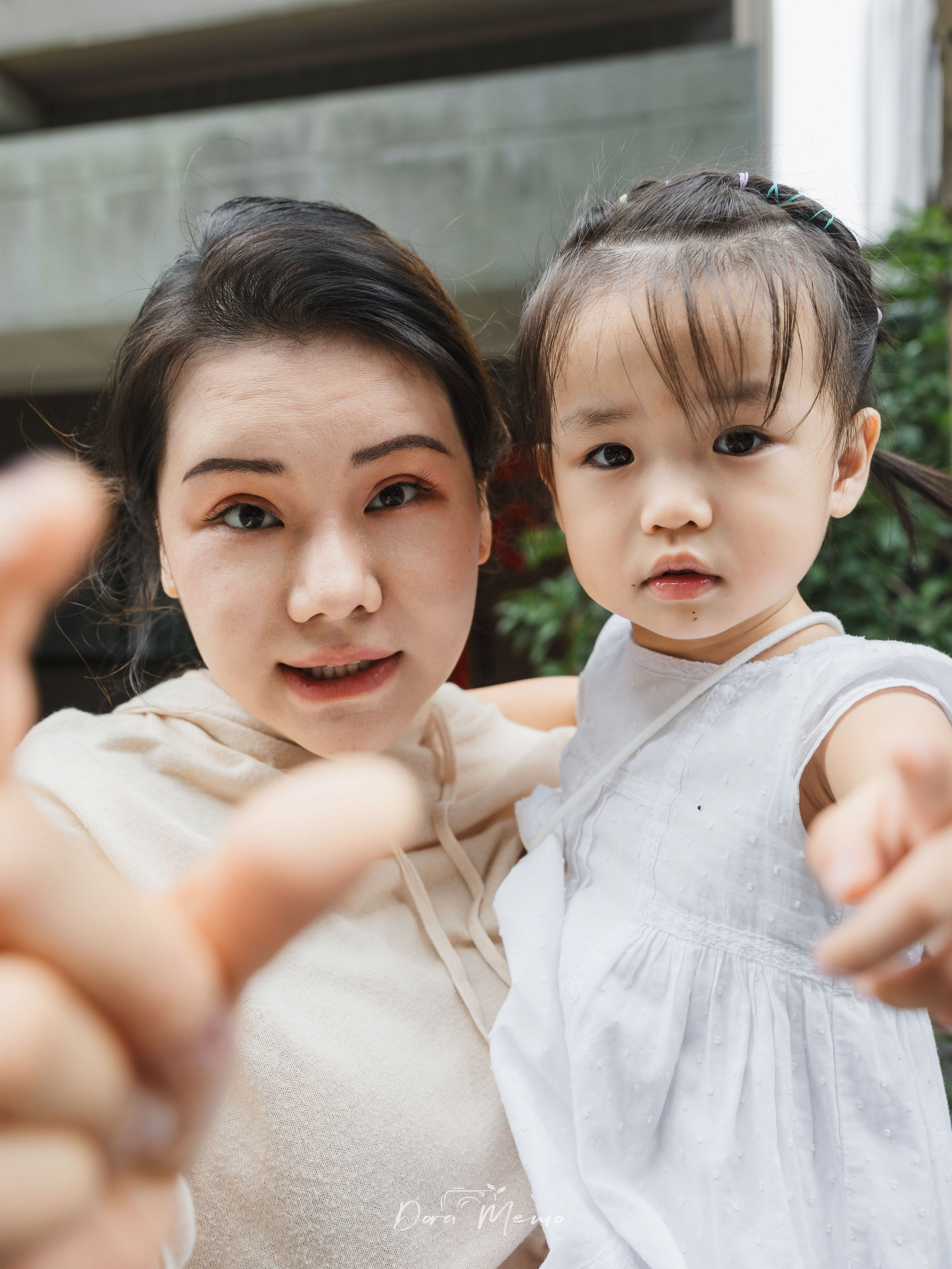 Mother and young daughter reach toward the camera during a warm at-home family photography session.