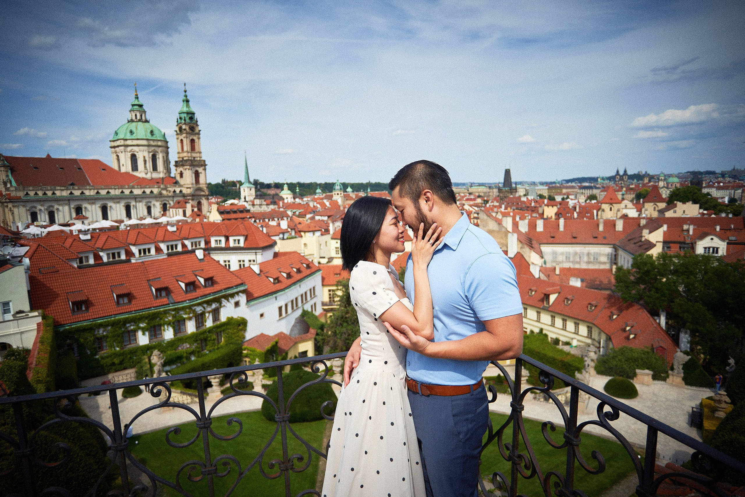Couple cuddling at the top terrace of Vrtba Garden overlooking Malá Strana's red rooftops, Prague.